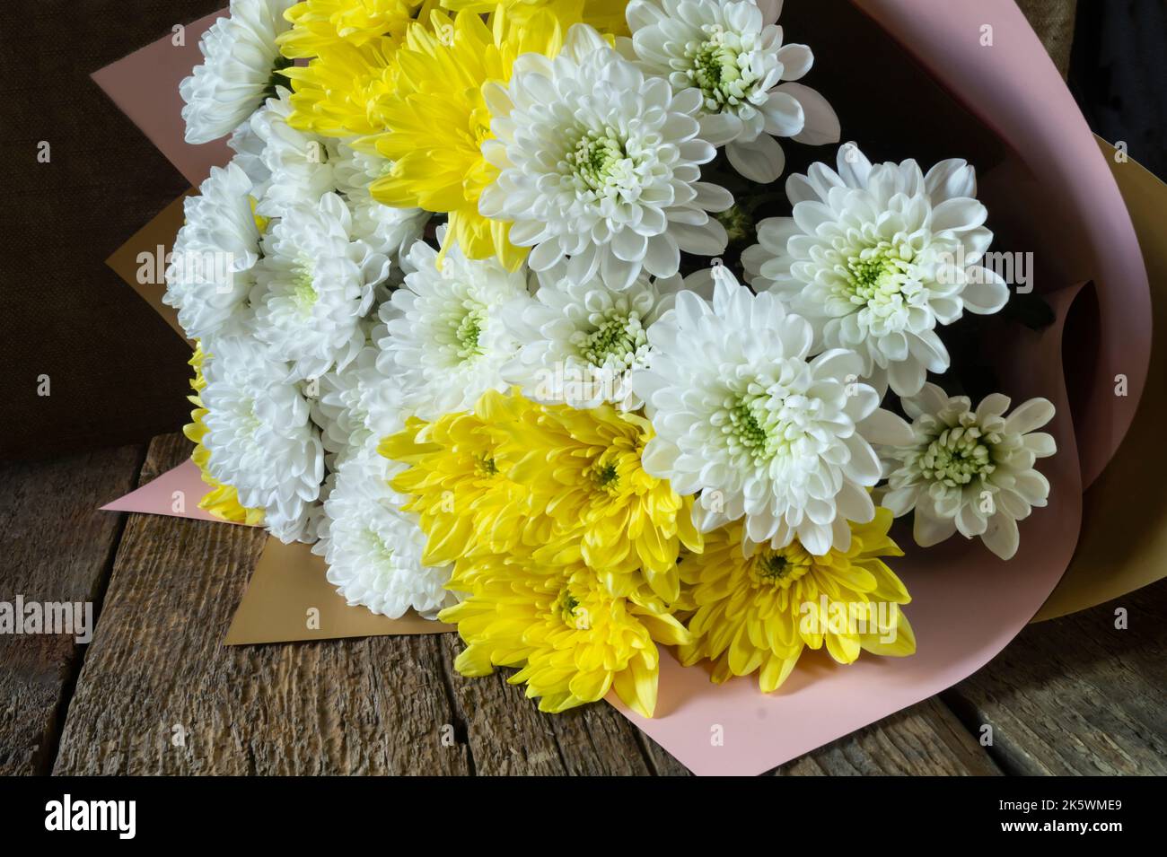Un bouquet di bellissimi fiori su un vecchio asse di legno. Crisantemi luminosi su sfondo scuro Foto Stock
