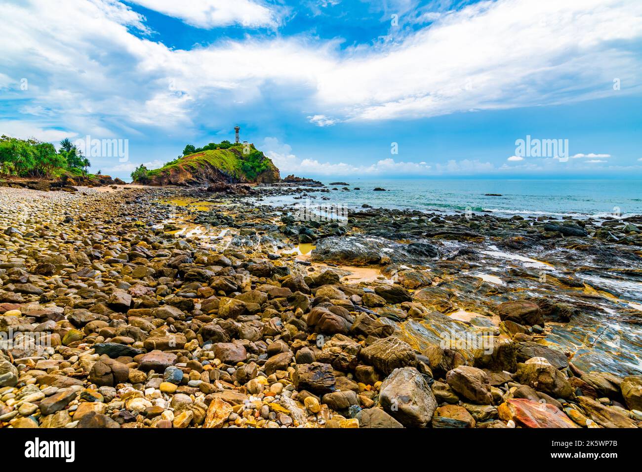 Faro sulla roccia al parco nazionale di Mu Ko Lanta, Thailandia. Vista dalla spiaggia con pietre. Estate tempo, cielo blu con nuvole. Foto Stock