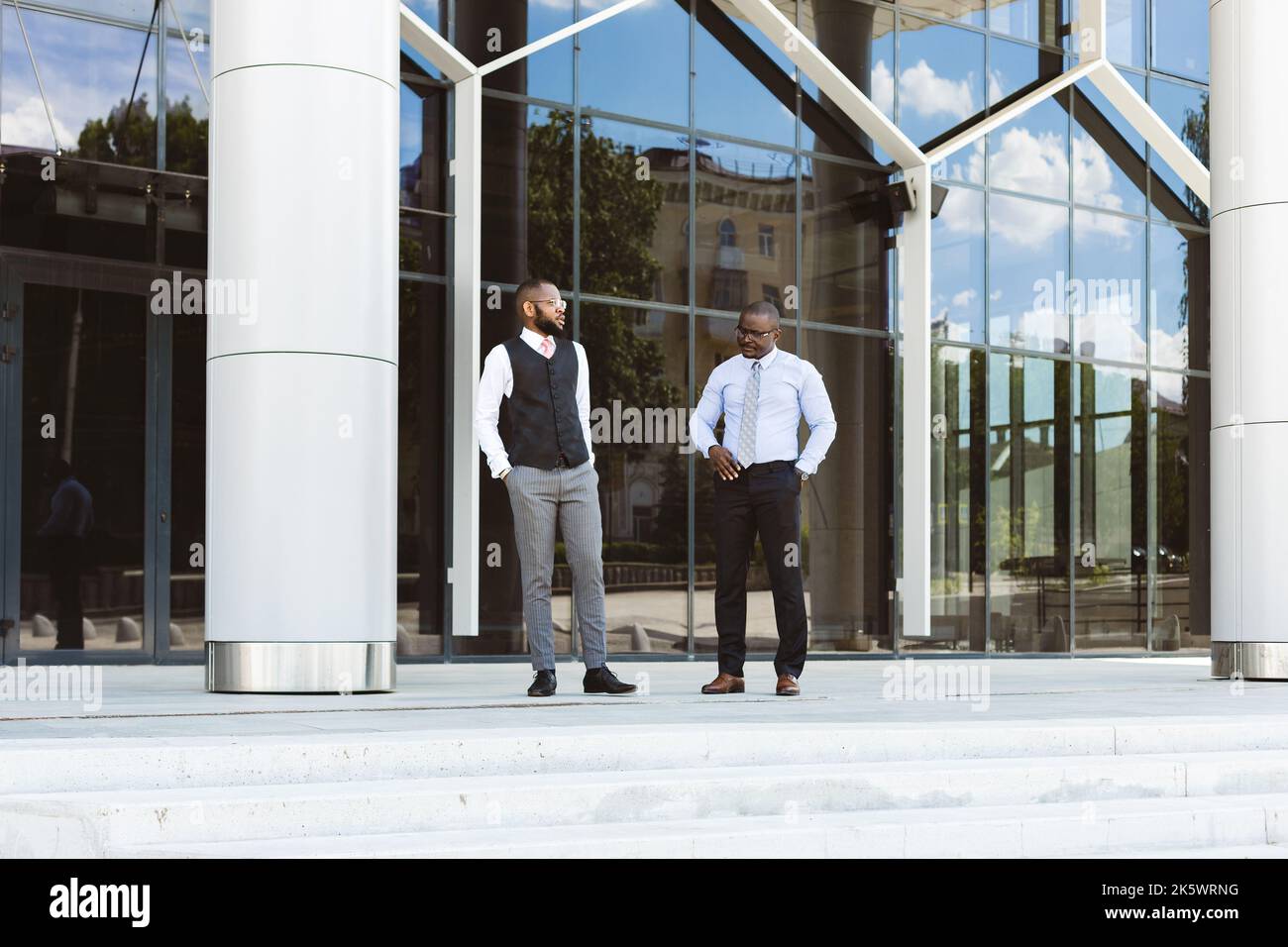 Ritratto di due uomini d'affari dalla pelle scura che camminano e parlano davanti ad un edificio moderno esterno. Meeting all'aperto Foto Stock