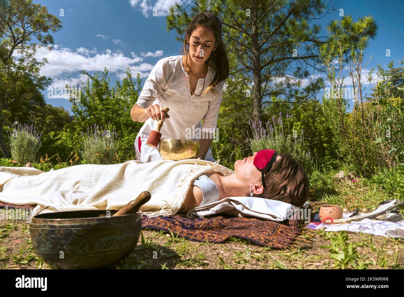 Terapista donna che pratica la terapia di guarigione del suono su una donna che giace in un ambiente naturale. Foto Stock
