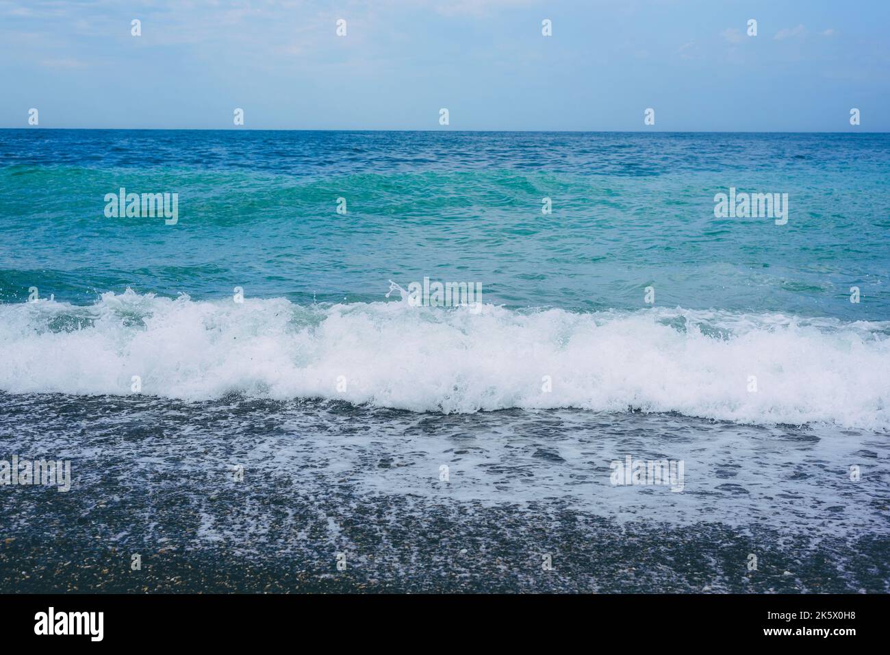 Spiaggia di ciottoli bagnata da onde di mare tempestose contro il cielo blu Foto Stock