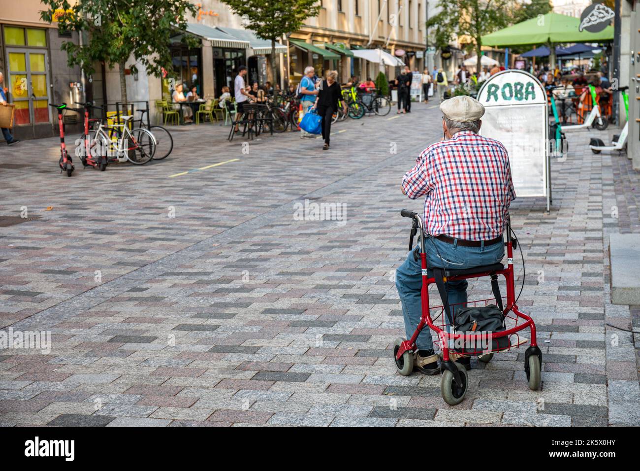 Uomo anziano seduto su un rullo o su un aiuto per camminare nella zona pedonale ISO Roobertinkatu, quartiere Punavuori di Helsinki, Finlandia Foto Stock