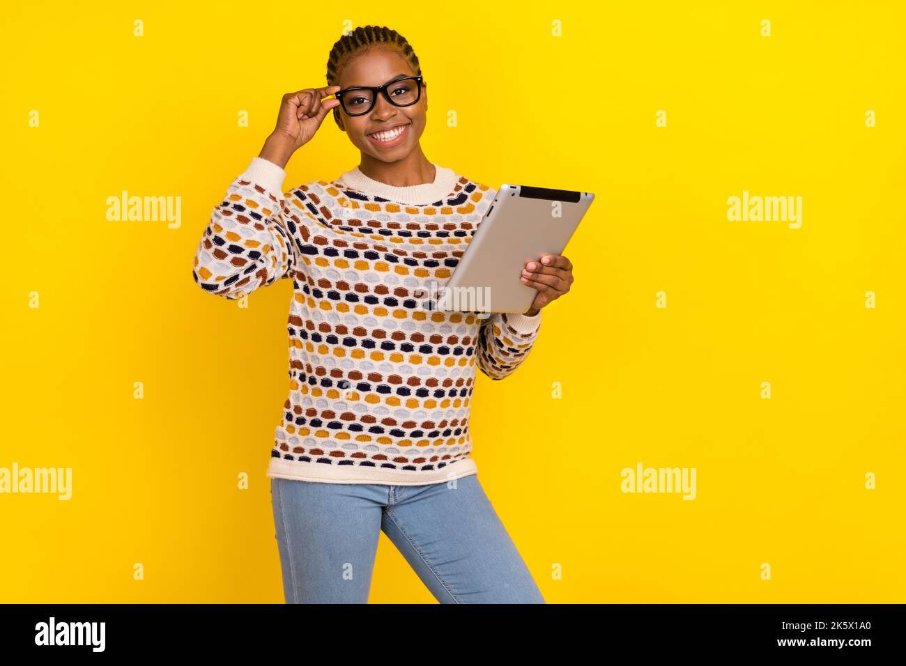 Foto di giovane fidata ragazza con cornrows vestita stampa jumper tenere occhiali da tablet isolato su sfondo di colore giallo brillante Foto Stock
