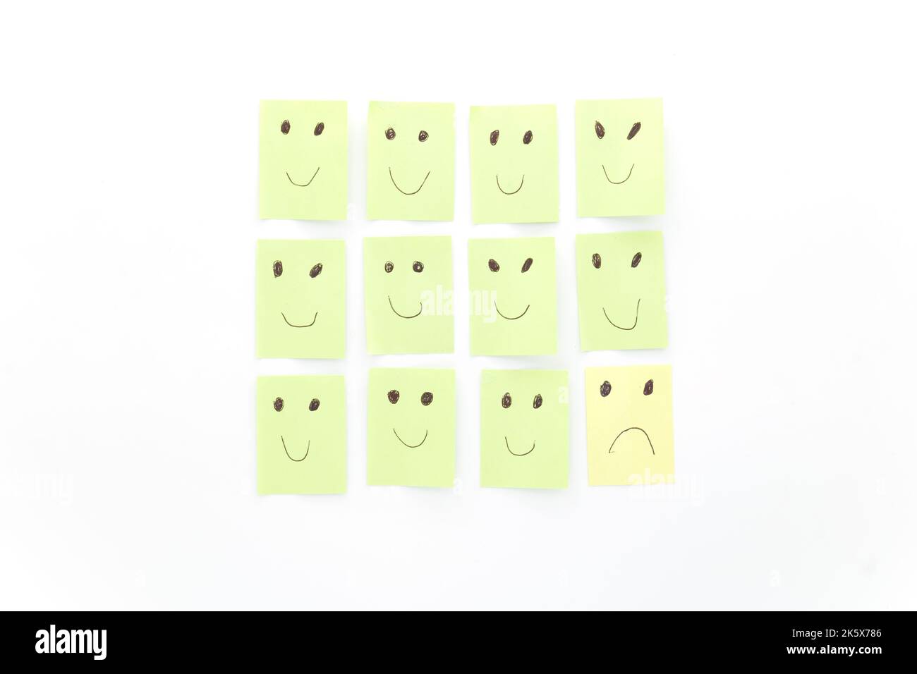 Immagine concettuale di essere triste tra gli altri felici. Soddisfatto, deluso. Note adesive verdi e gialle isolate su sfondo bianco. Foto Stock