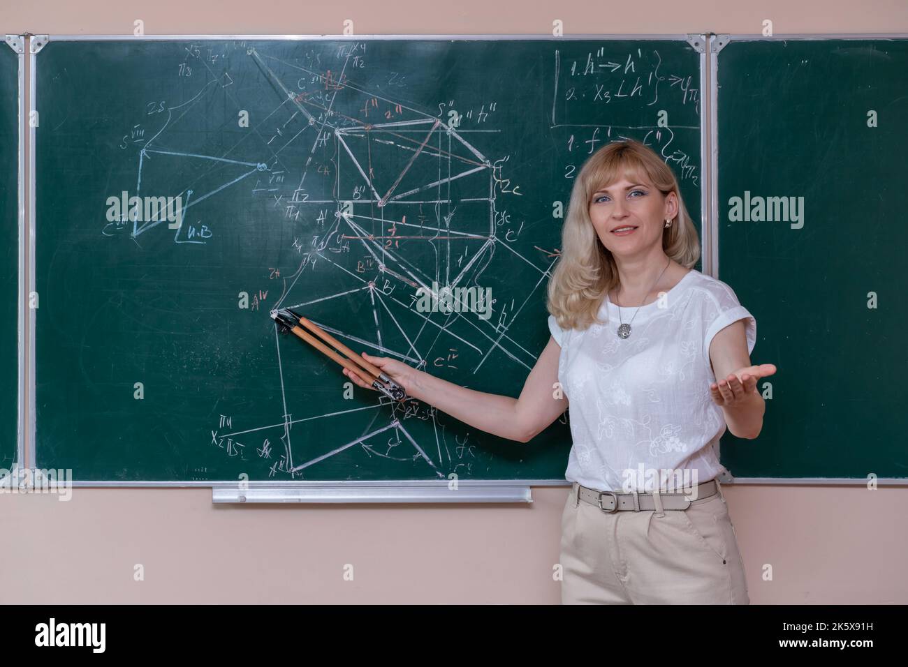 Una giovane maestra di matematica caucasica si trova nella lavagna e spiega la soluzione di un problema matematico Foto Stock