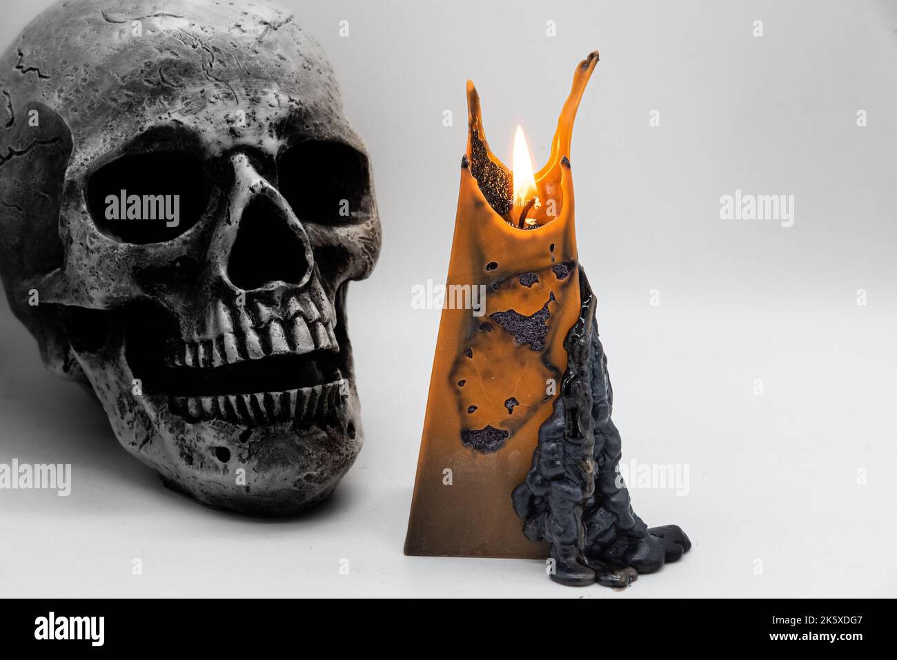 Una candela gialla di Halloween e un vecchio cranio su uno sfondo bianco Foto Stock