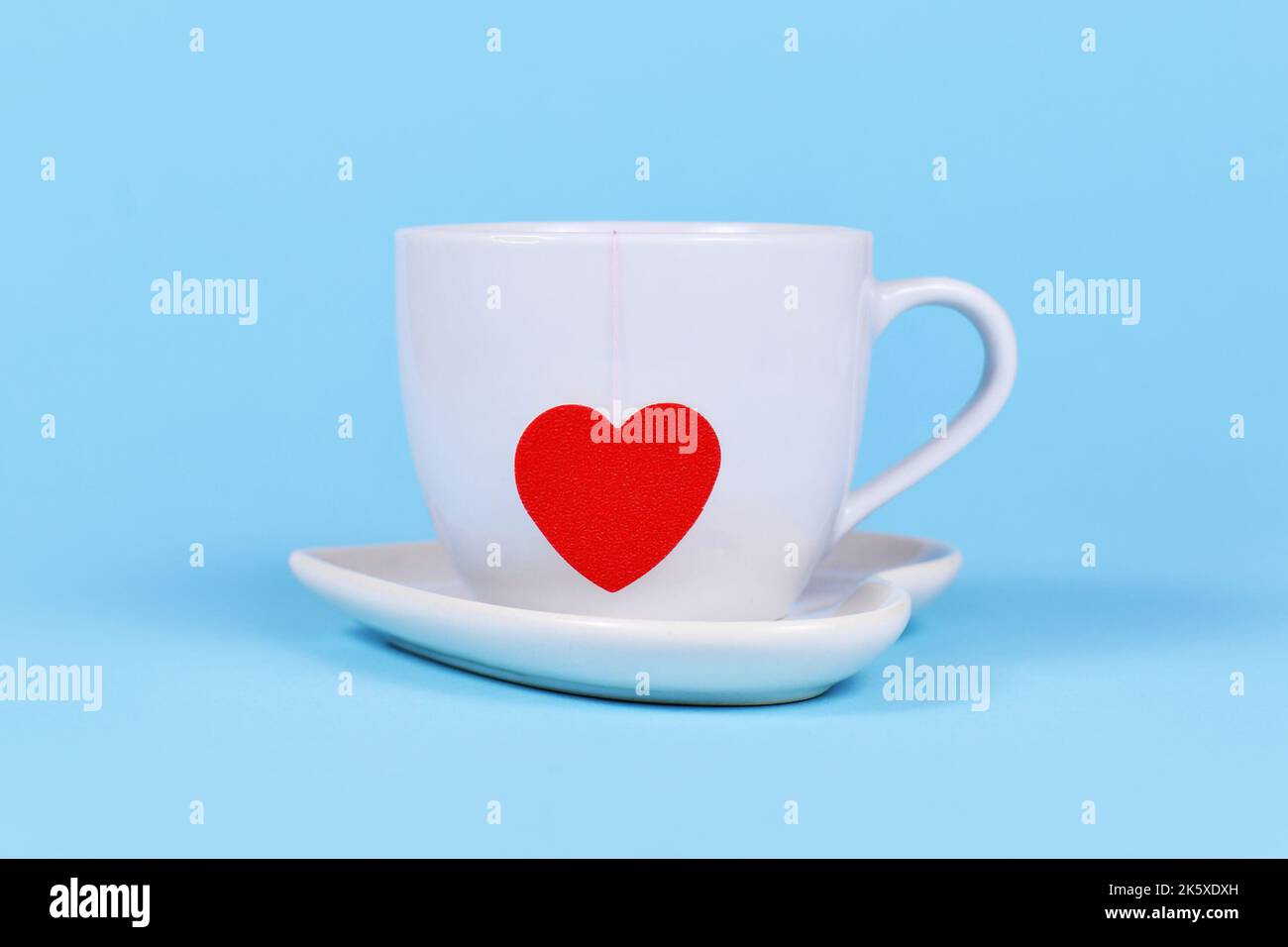 Tazza da tè bianca con sacchetto di carta da tè a forma di cuore rosso su sfondo blu Foto Stock
