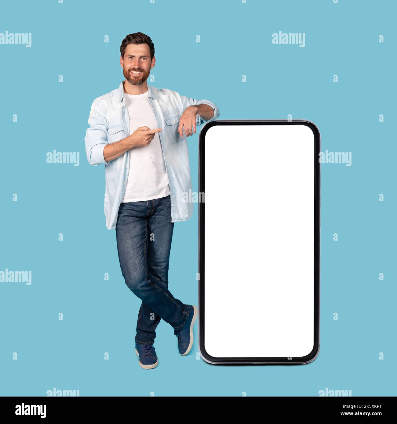 Allegro uomo caucasico millenario punta il dito contro l'enorme smartphone con schermo vuoto Foto Stock