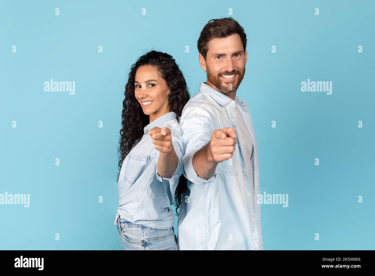 Sorridente maschio caucasico millenario con barba e femmina medio orientale in casual show dita alla macchina fotografica Foto Stock