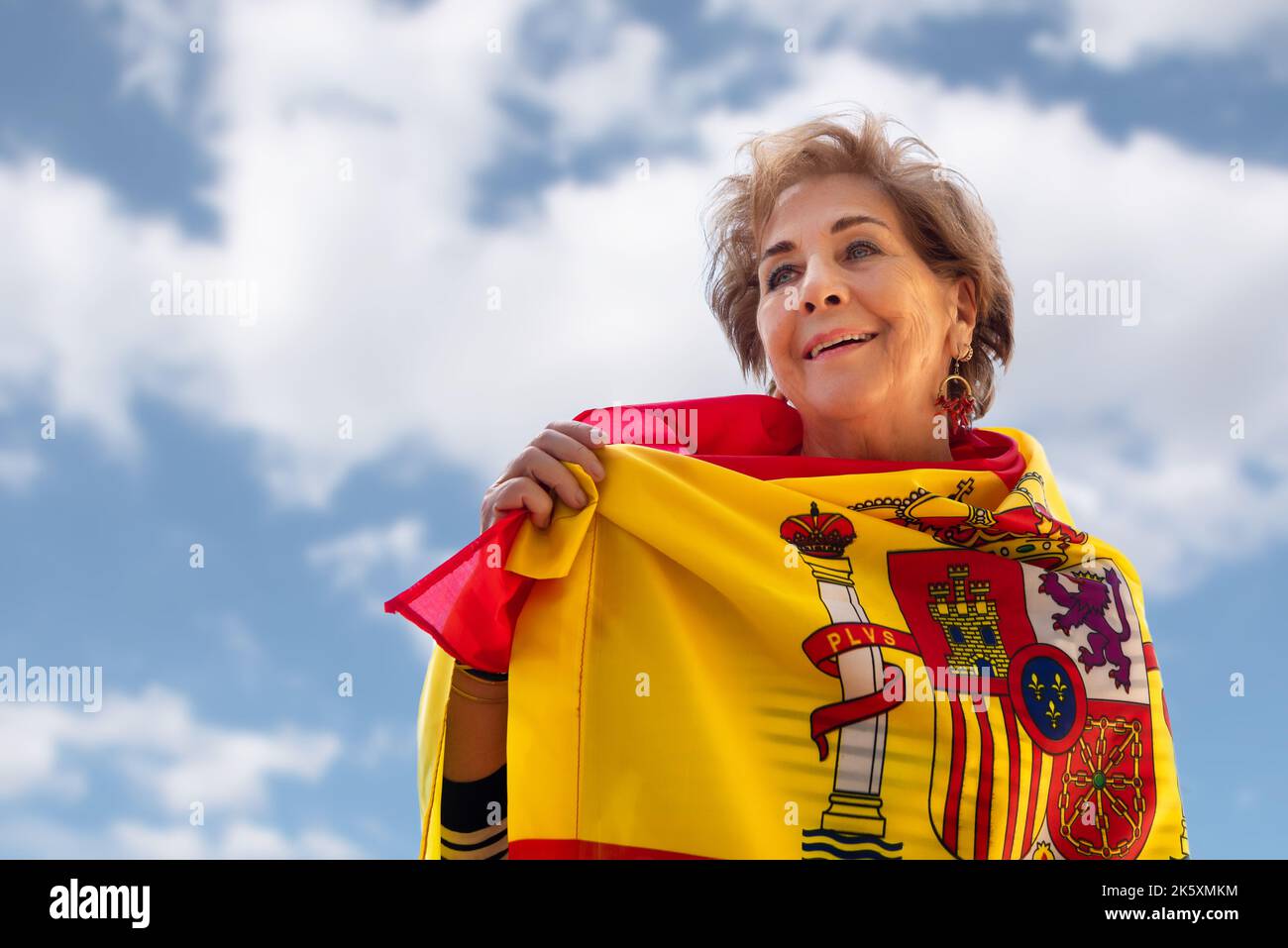 Donna anziana sorridente, circondata dalla bandiera di Spagna su uno sfondo blu con nuvole. Orgoglio di essere spagnolo. Amore e patriottismo. Columbus giorno Foto Stock