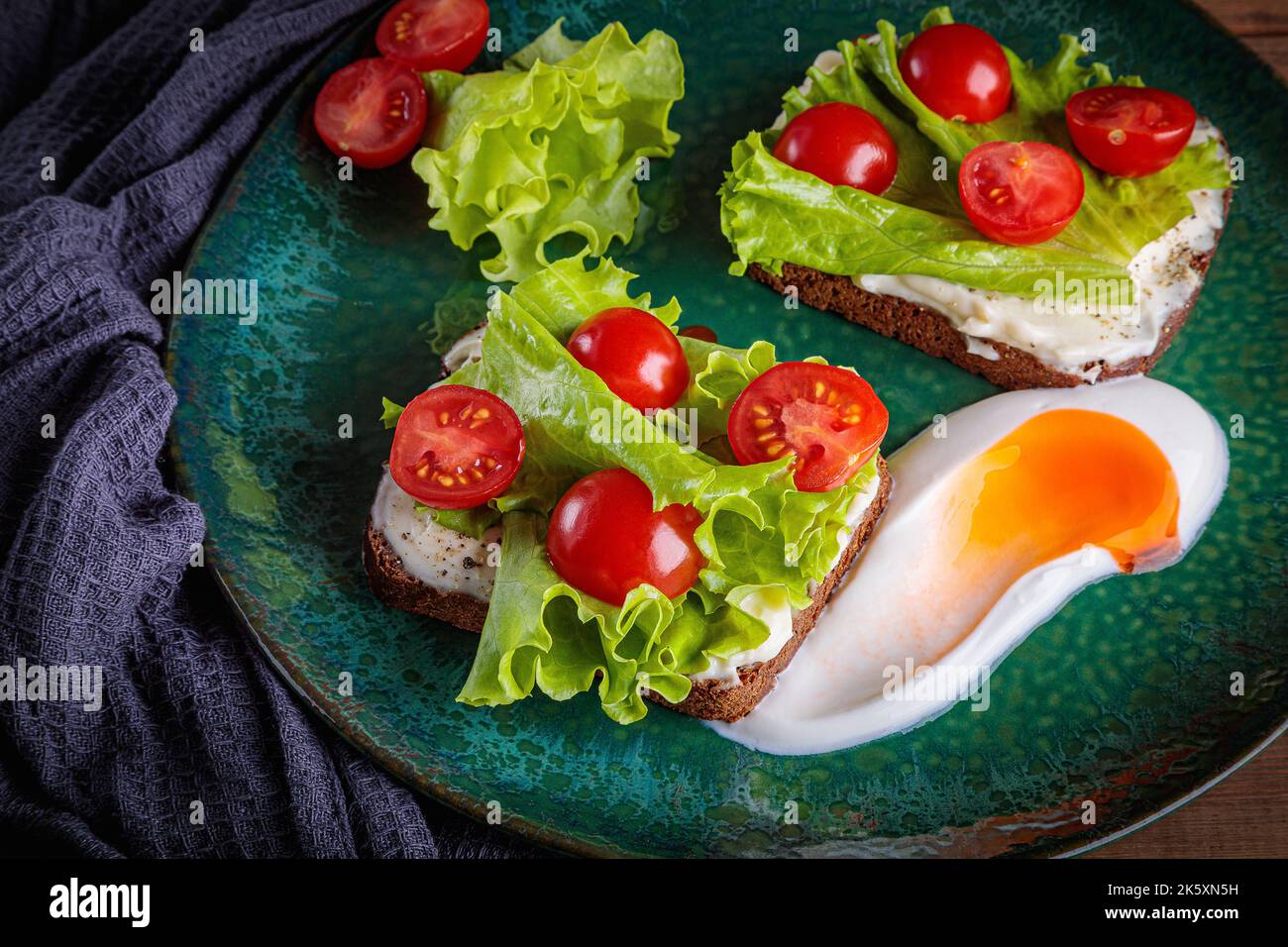 Panino nero con insalata di formaggio fuso e pomodori su un piatto verde Foto Stock