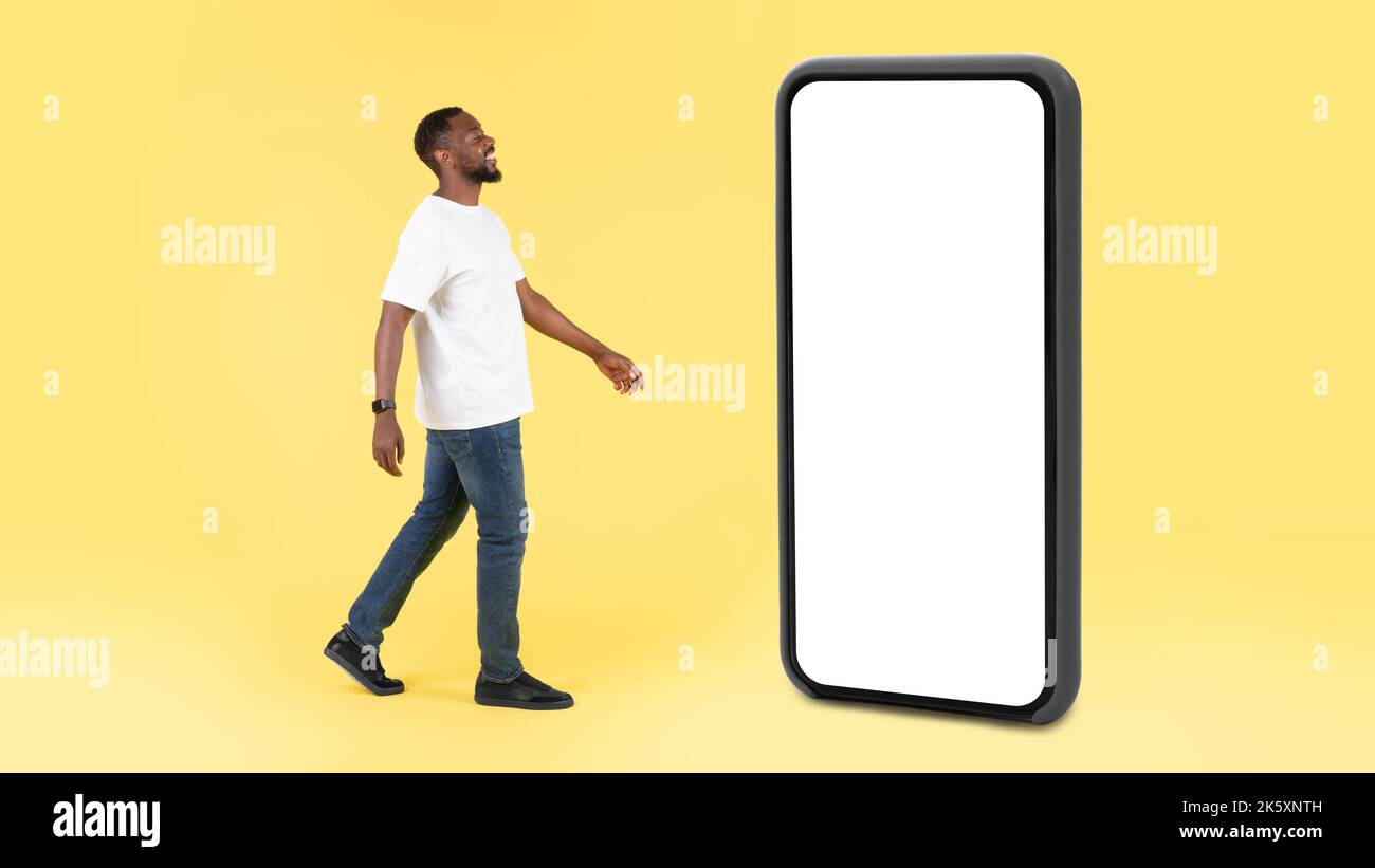 Ragazzo nero a piedi vicino enorme schermo del telefono su sfondo giallo Foto Stock