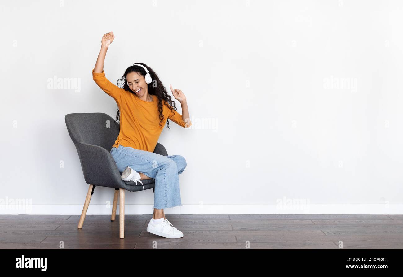 Giovane donna allegra seduta su poltrona, ascoltando musica Foto Stock