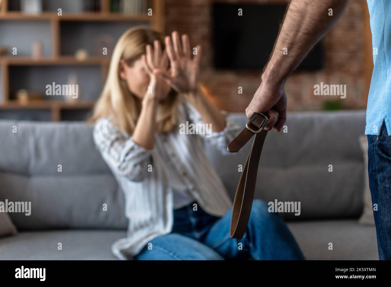 Disperata donna europea di mezza età che soffre di battere da un uomo aggressivo con la cintura in soggiorno Foto Stock