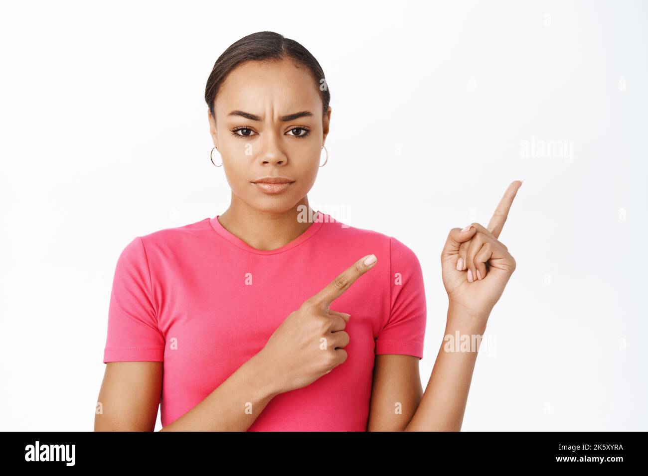 Primo piano della donna nera rovesciato, puntando le dita a destra, mostrando la pubblicità con il volto deluso, in piedi su sfondo bianco Foto Stock