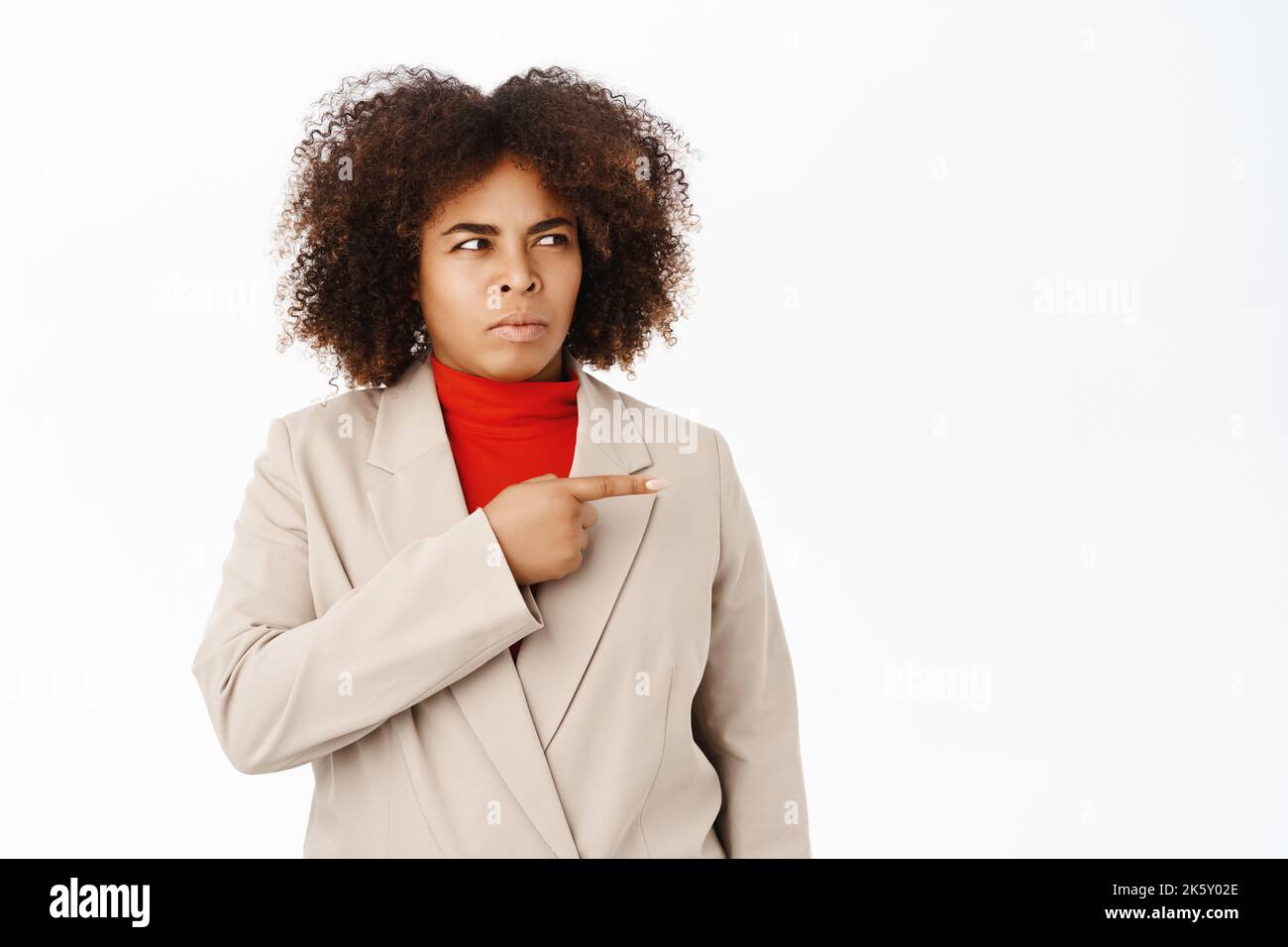 Immagine di nero businesswoman, sembra sospettoso, punta a destra e guarda con incredulità, si erge su sfondo bianco Foto Stock