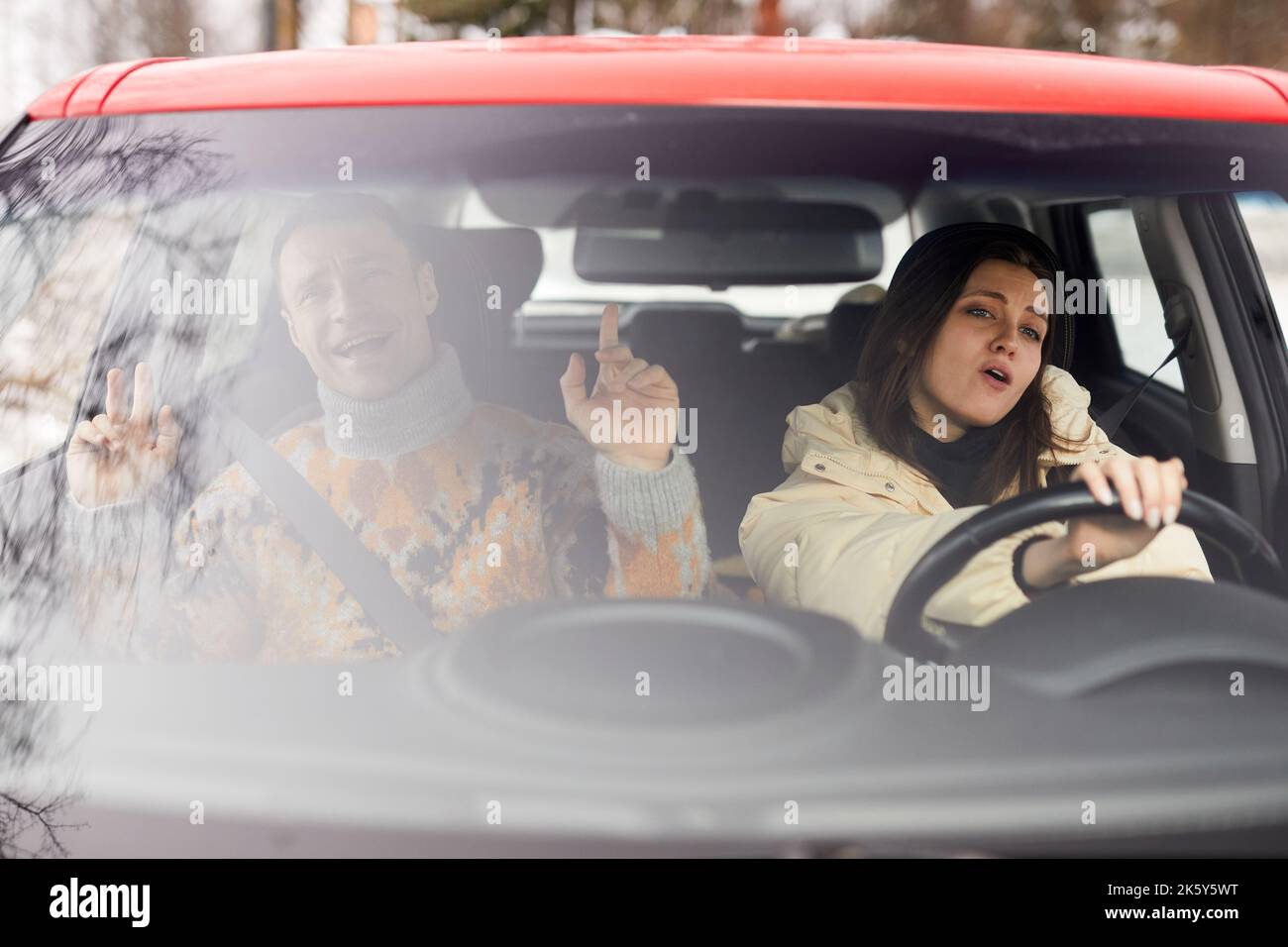 Ritratto di giovane coppia spensierata che canta in auto mentre guida per vacanze invernali insieme Foto Stock