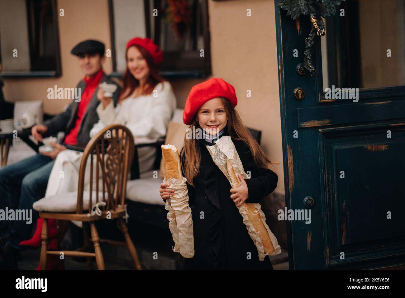 Una ragazza alla moda con baguette si trova vicino al negozio sullo sfondo dei suoi genitori. Foto Stock