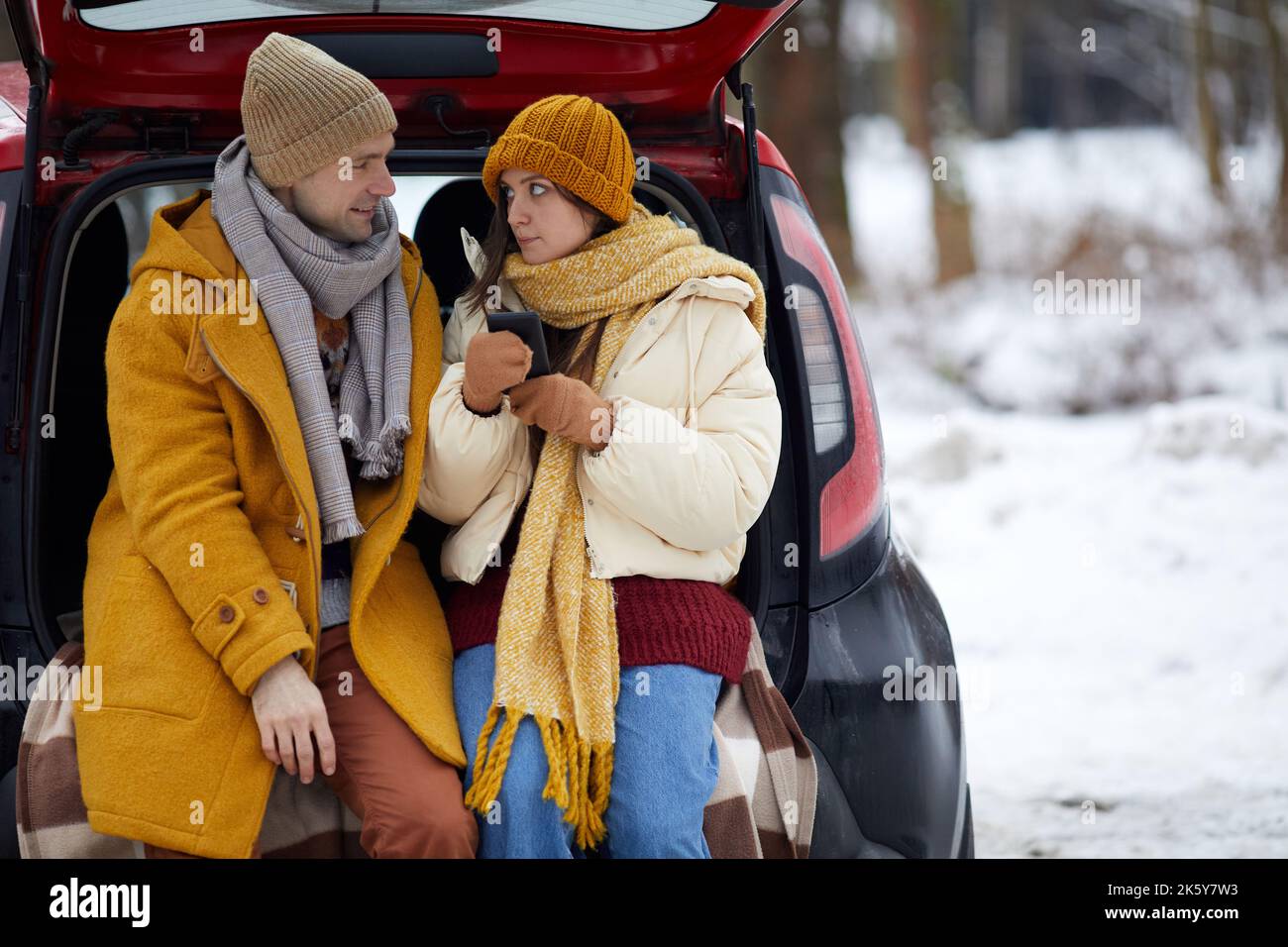 Ritratto di giovane coppia seduta in tronco auto nella foresta invernale mentre godendo di viaggio per le vacanze, copia spazio Foto Stock