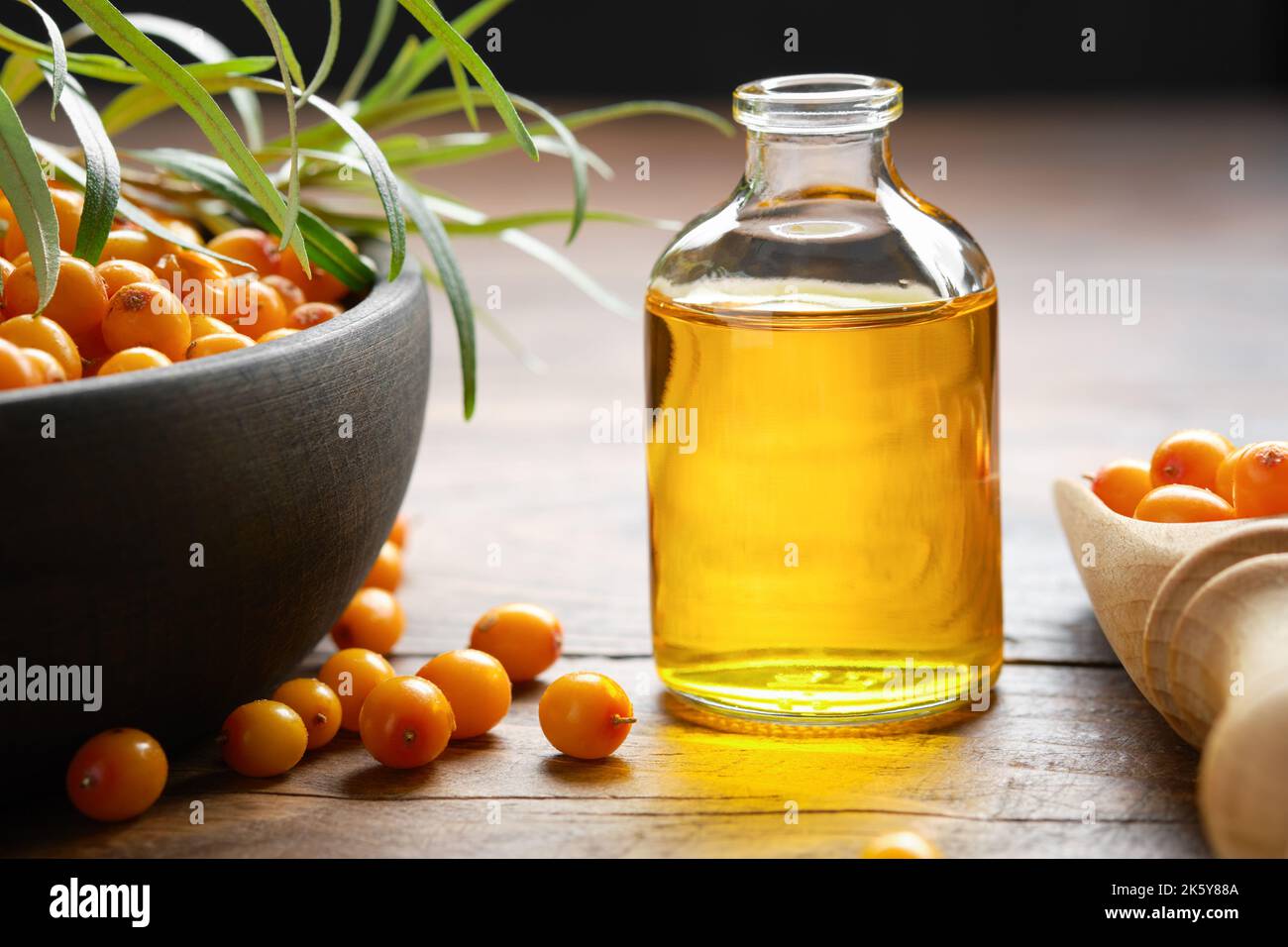 Bottiglia di olio essenziale di biancospino, ciotola di bacche di biancospino, cucchiaio di legno di bacche di biancospino. Foto Stock