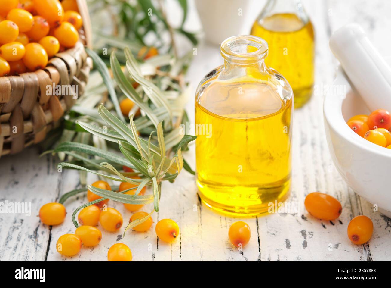 Bottiglie di olio essenziale di biancospino marino, mortaio e cesto di bacche di biancospino. Foto Stock