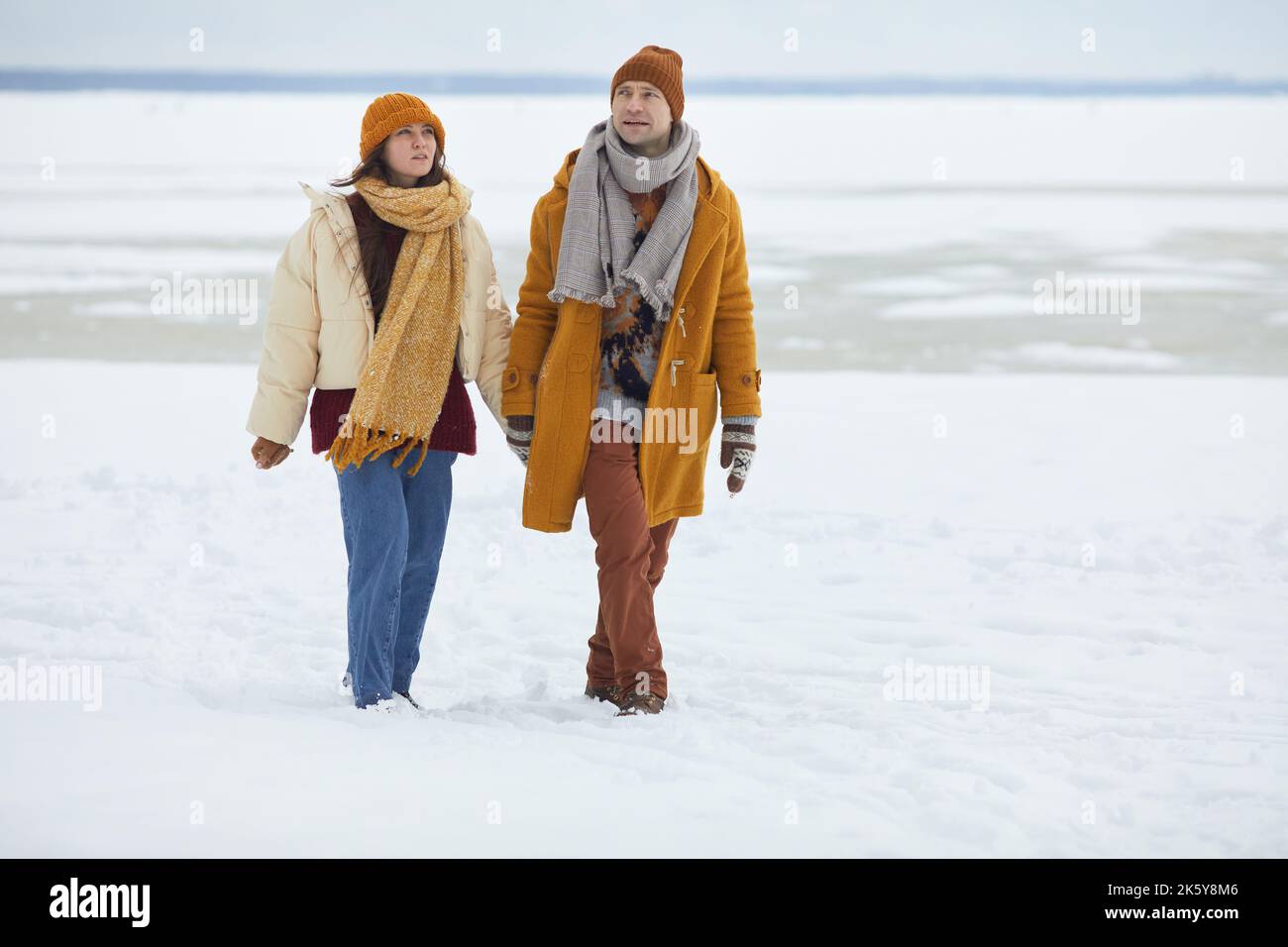Ritratto a tutta lunghezza di una giovane coppia che tiene le mani e cammina verso la fotocamera in un paesaggio invernale minimo, spazio di copia Foto Stock