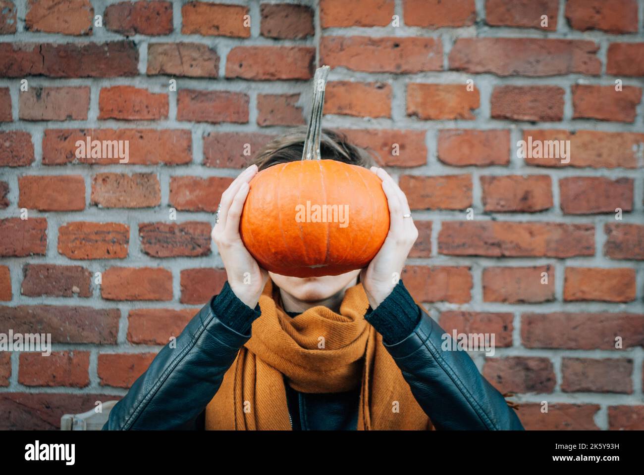 Donna tiene una zucca contro il suo volto in piedi contro un muro di mattoni Foto Stock