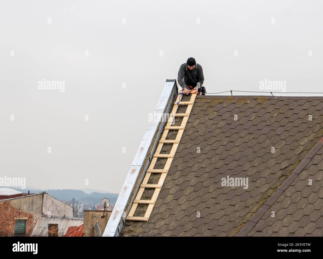 Un riparatore con una scala sta riparando il tetto Foto Stock