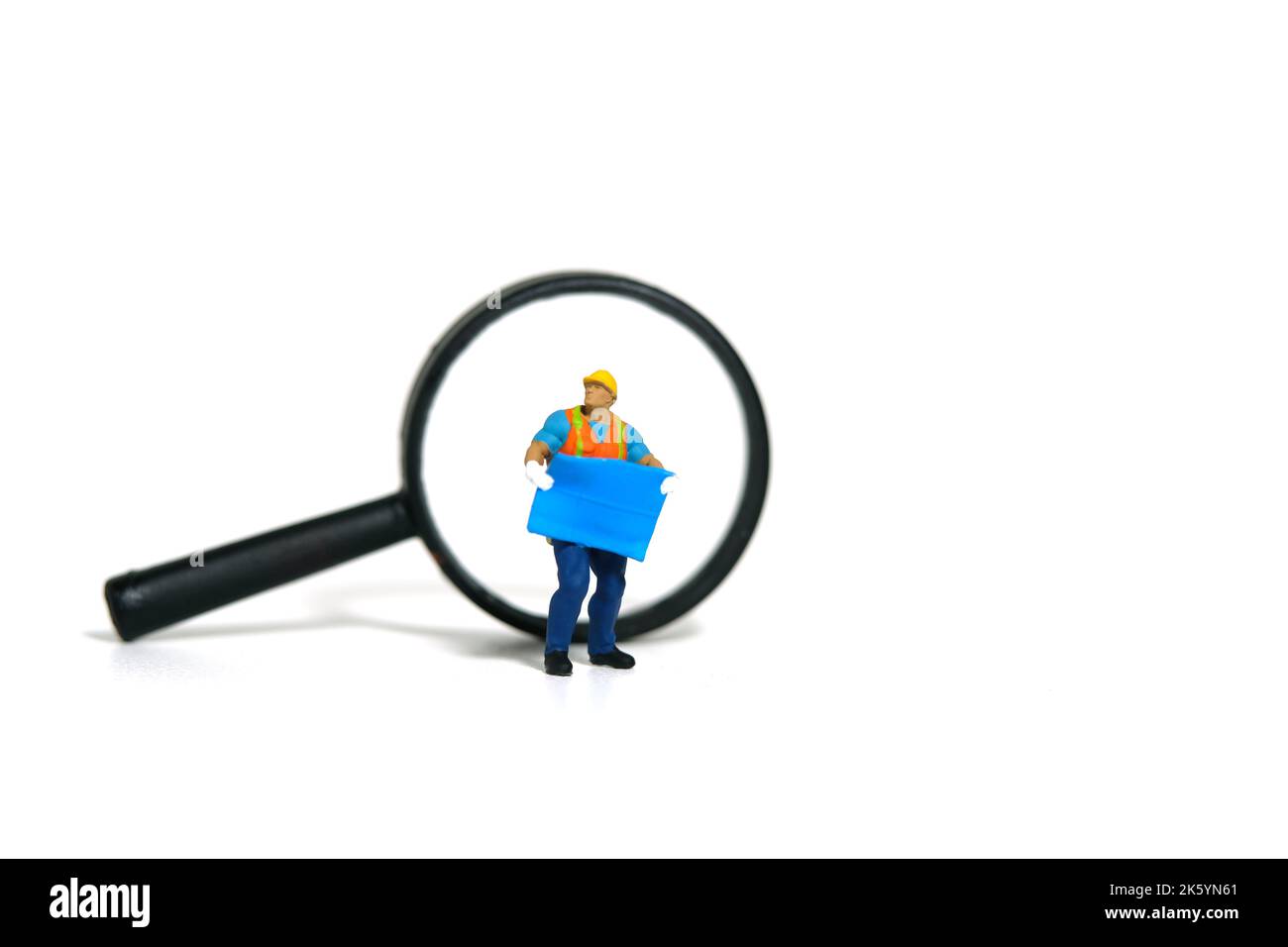 Fotografia di figura giocattolo delle persone in miniatura. Concetto di determinazione della posizione del progetto. Un lavoratore di costruzione che tiene il BluePrint con la lente di ingrandimento. Isolare Foto Stock