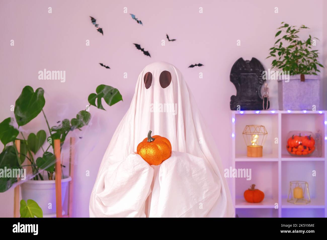 Divertente concetto di Halloween. Un grande fantasma tiene in mano una zucca di Halloween arancione. Uno studio di Halloween girato con un bellissimo sfondo. Luce al neon. Foto Stock
