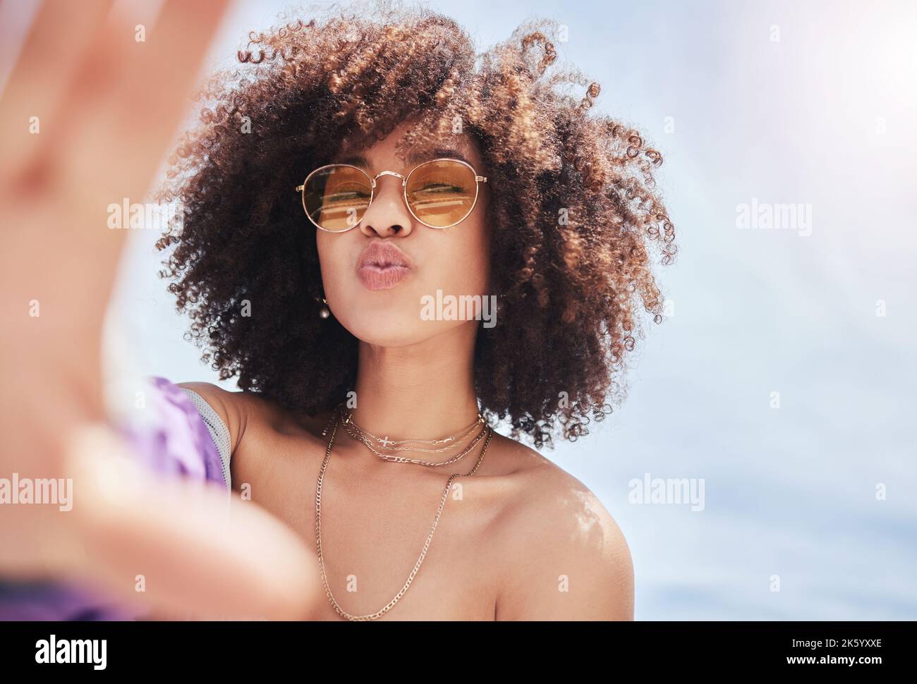 Ritratto di giovane donna alla moda bella gara mista con un afro sorridente e in posa per un selfie all'esterno. Donna ispanica che indossa occhiali da sole che guarda Foto Stock