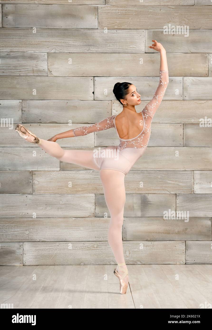 Corpo pieno di ballerina femminile snella in tuta da bodysuit in piedi su scarpe a punta con gamba sollevata durante le prove in studio Foto Stock