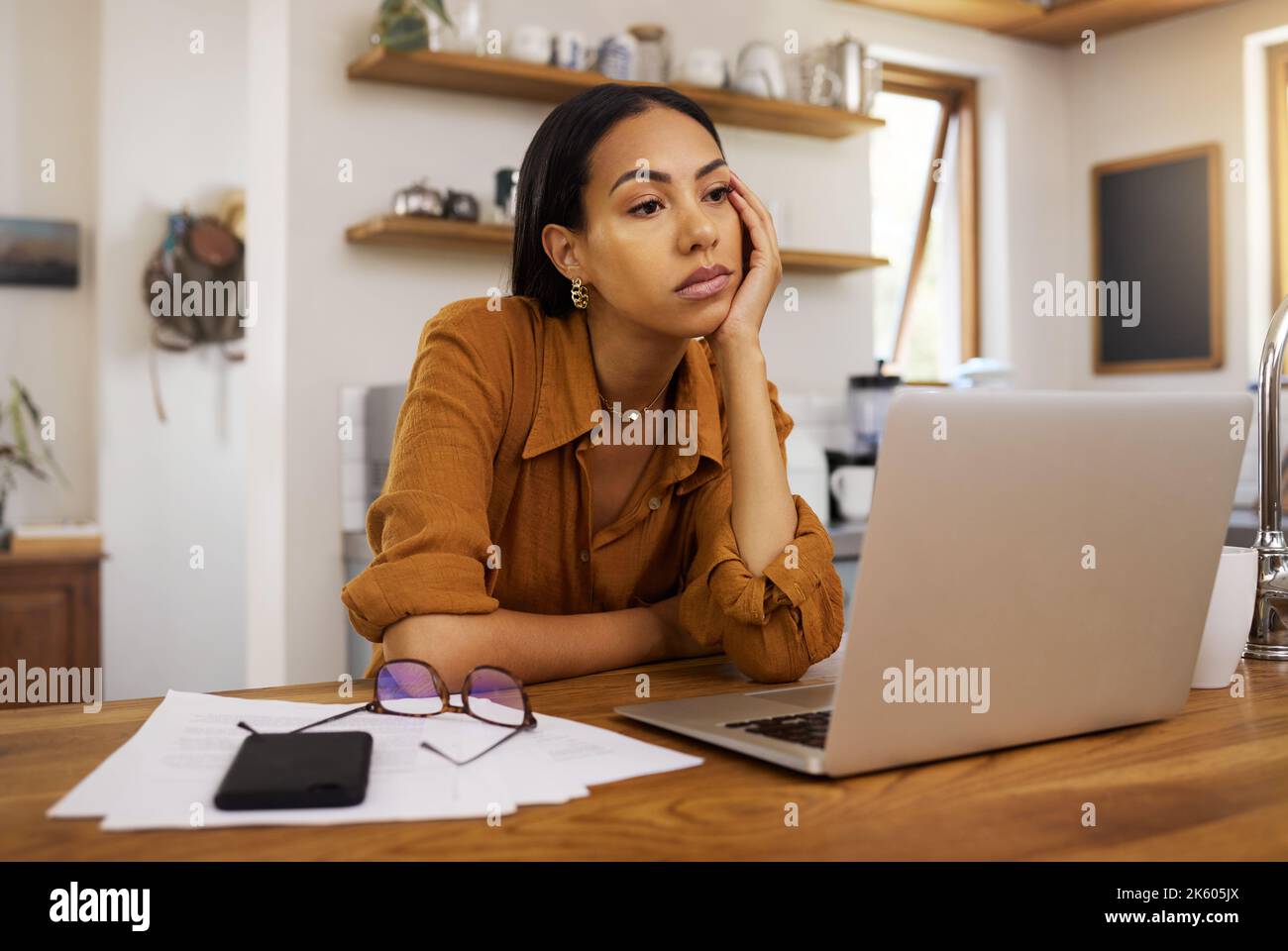 Annoiata donna d'affari di corsa mista che passa attraverso la carta e le fatture e che lavora su un portatile a casa. Donna di affari ispanica stanco pensando mentre Foto Stock