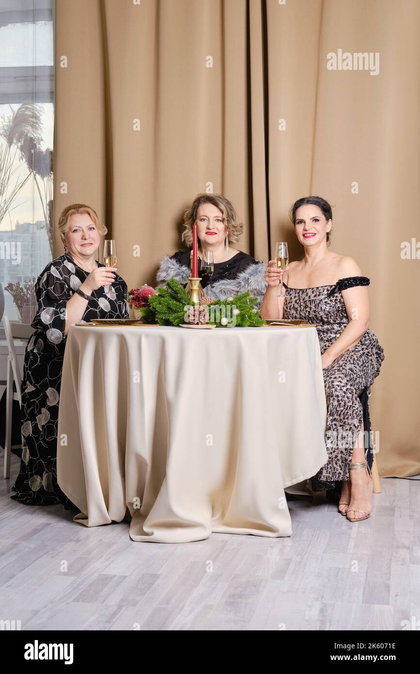 Tre donne gioiose di mezza età che festeggiano il natale seduti dietro il tavolo delle feste Foto Stock