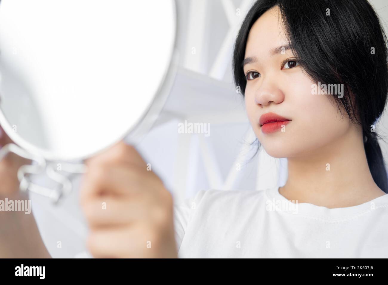 Bellezza asiatica. Cura della pelle femminile. Procedura Spa. Trattamento idratante. Bella donna giapponese guardando uno specchio rotondo in camera luce interno. Foto Stock