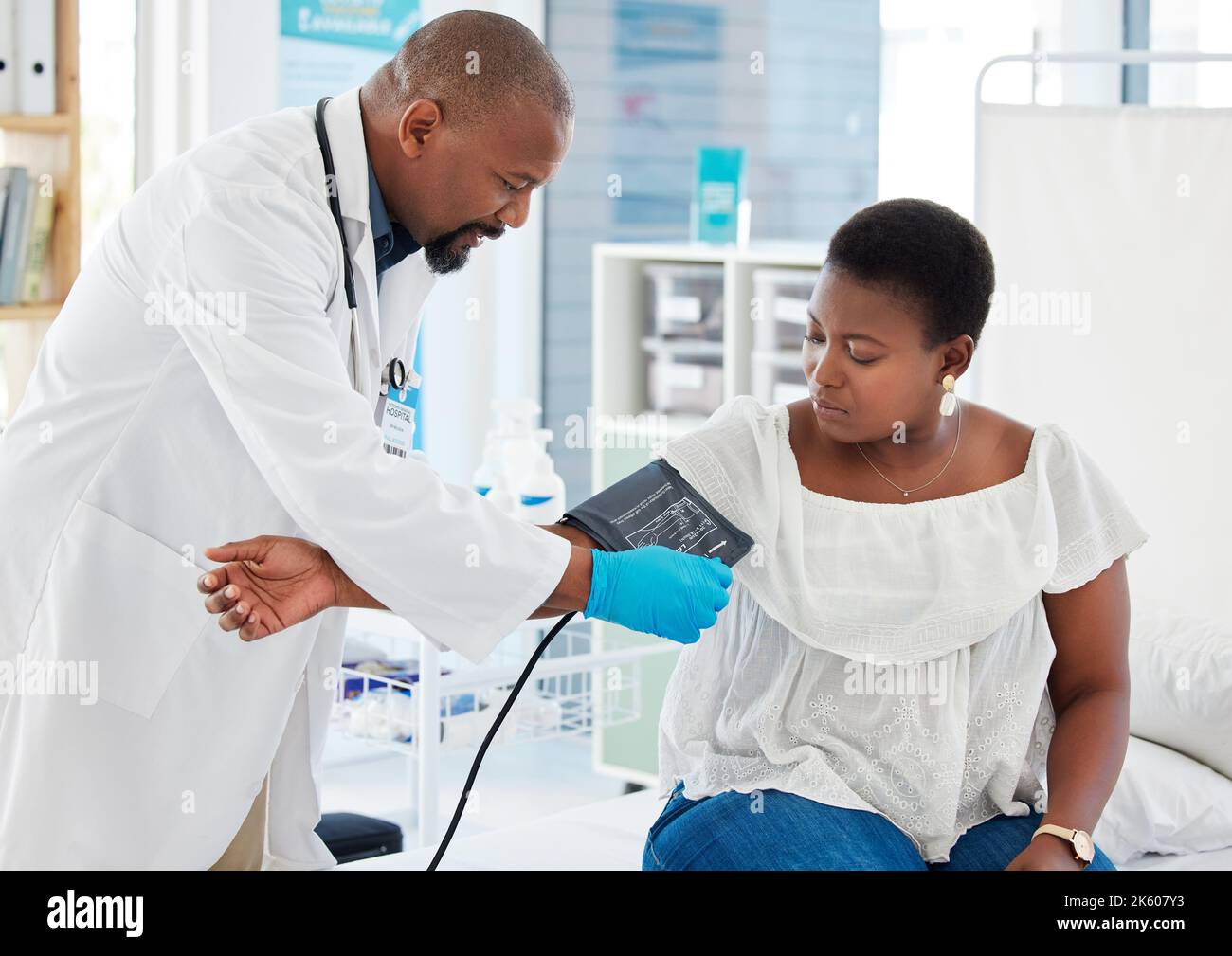 Medico maturo che controlla la pressione sanguigna di un paziente. Medico afro-americano che applica il bracciale per la pressione sanguigna. Dipendente medico in consultazione con Foto Stock