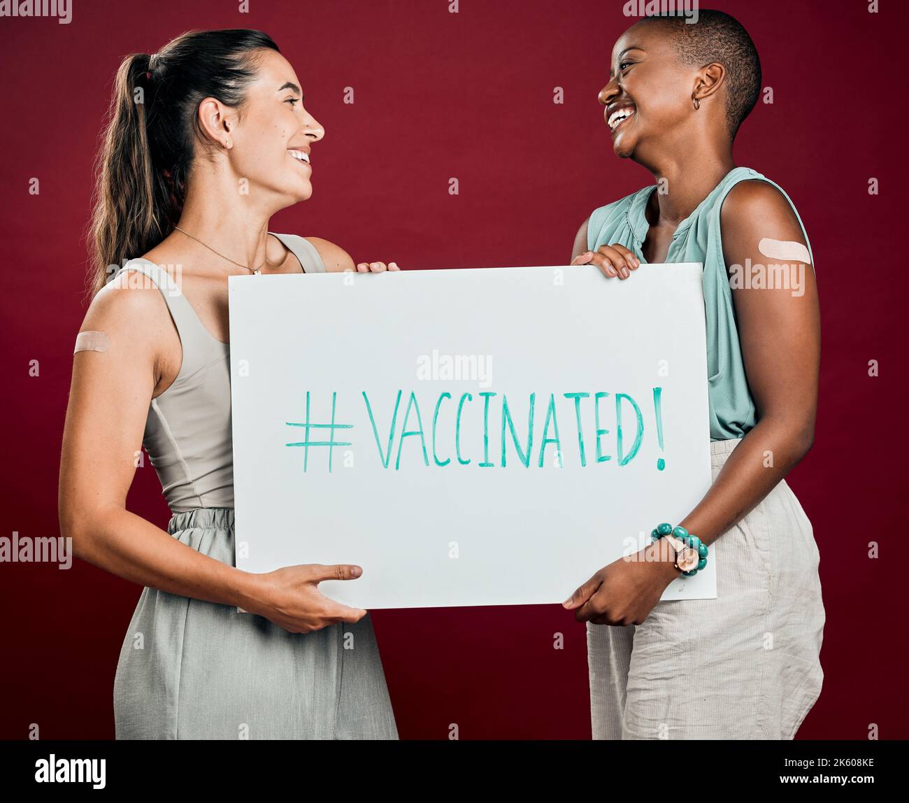 Covid ha vaccinato le donne di razza afro-americana e mista mostrando e tenendo il manifesto. Due persone isolate su sfondo rosso studio con copyspace Foto Stock