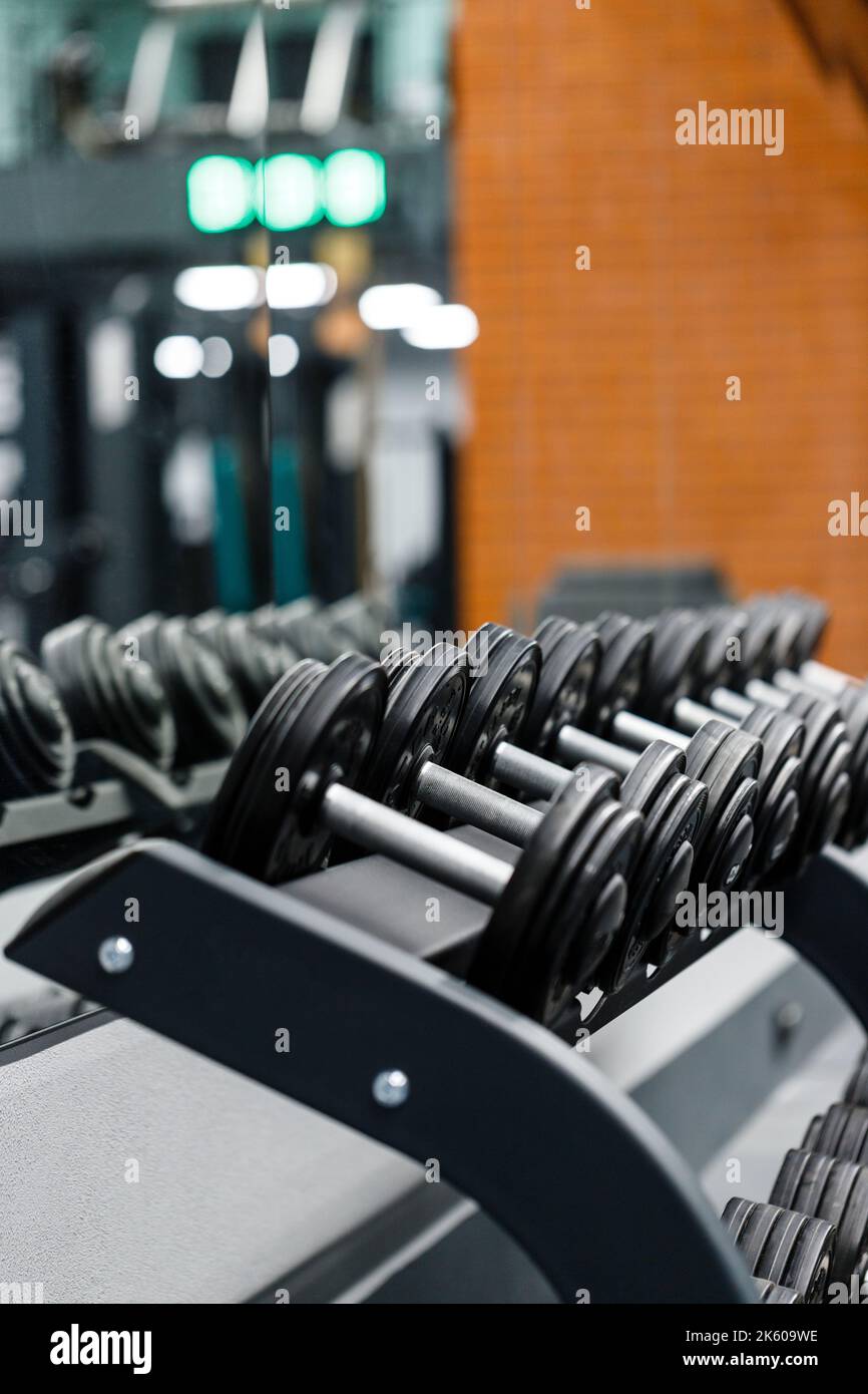 Primo piano di manubri in acciaio nero su scaffale nel centro fitness sportivo. I manubri in fila sono pronti per l'uso da parte degli atleti. Allenamento e. Foto Stock