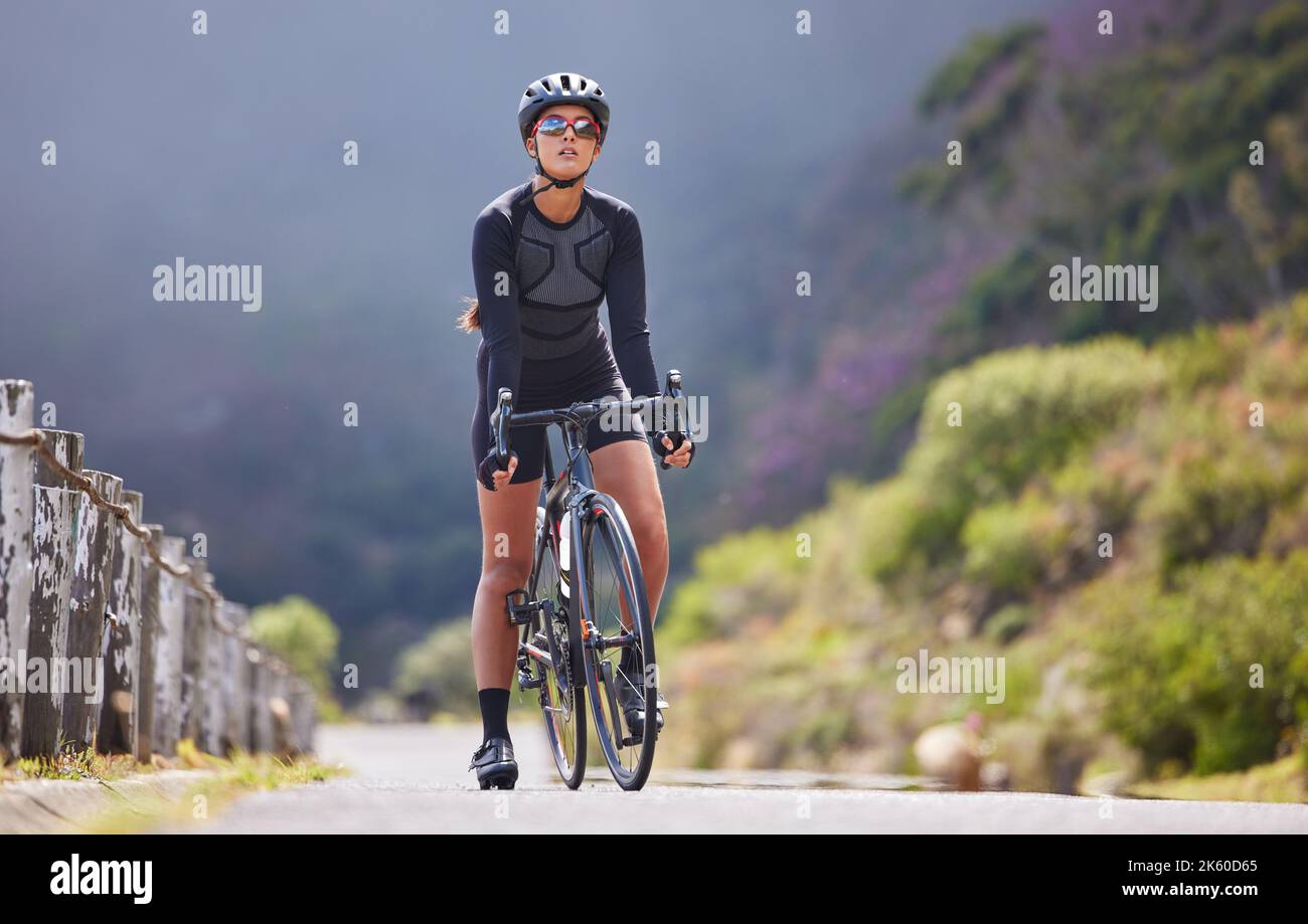 Una giovane atletica in bicicletta all'aperto. Donna sportiva indossando casco e occhiali mentre si guida una bicicletta su una strada lungo la montagna per l'esercizio Foto Stock