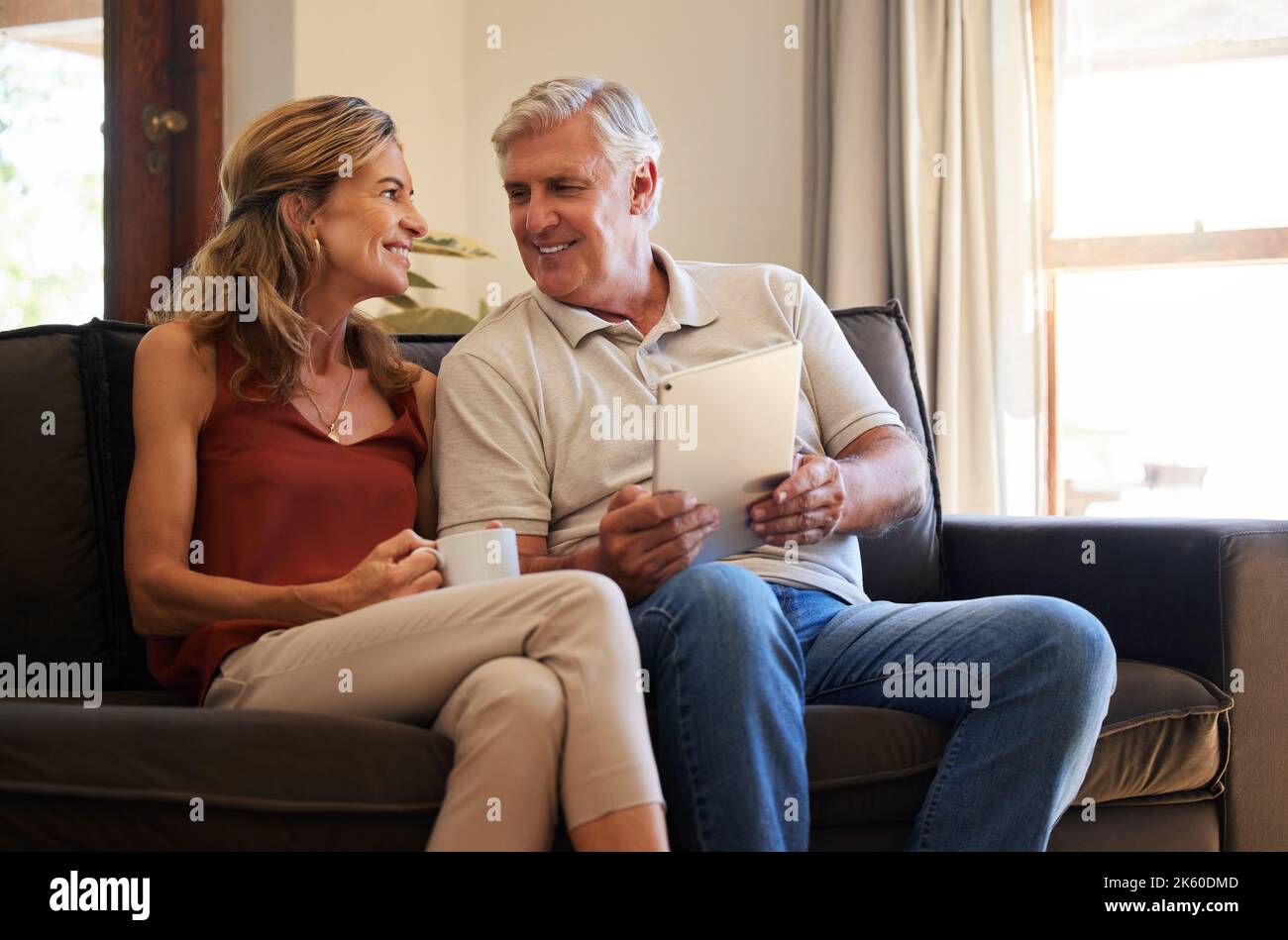 Tablet, social media e coppia senior sorridente per scegliere un film sul Web con caffè sul divano di casa. L'uomo e la donna anziani che parlano Foto Stock