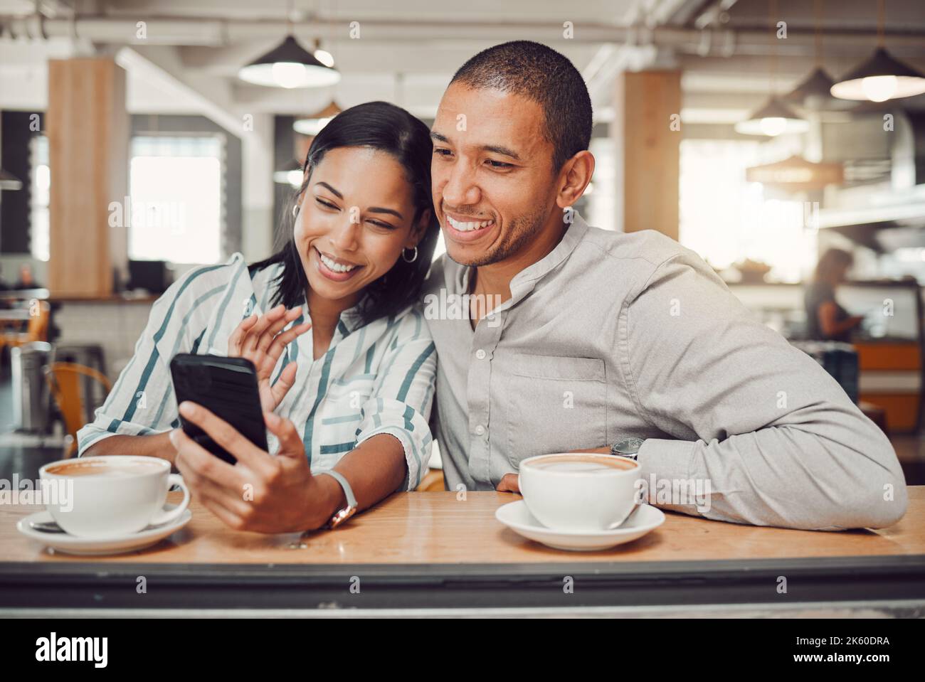 Felice giovane coppia di gara mista seduto al tavolo con un caffè mentre si guarda qualcosa sullo smartphone nel bar. Coppia amorevole sorridente mentre prende Foto Stock