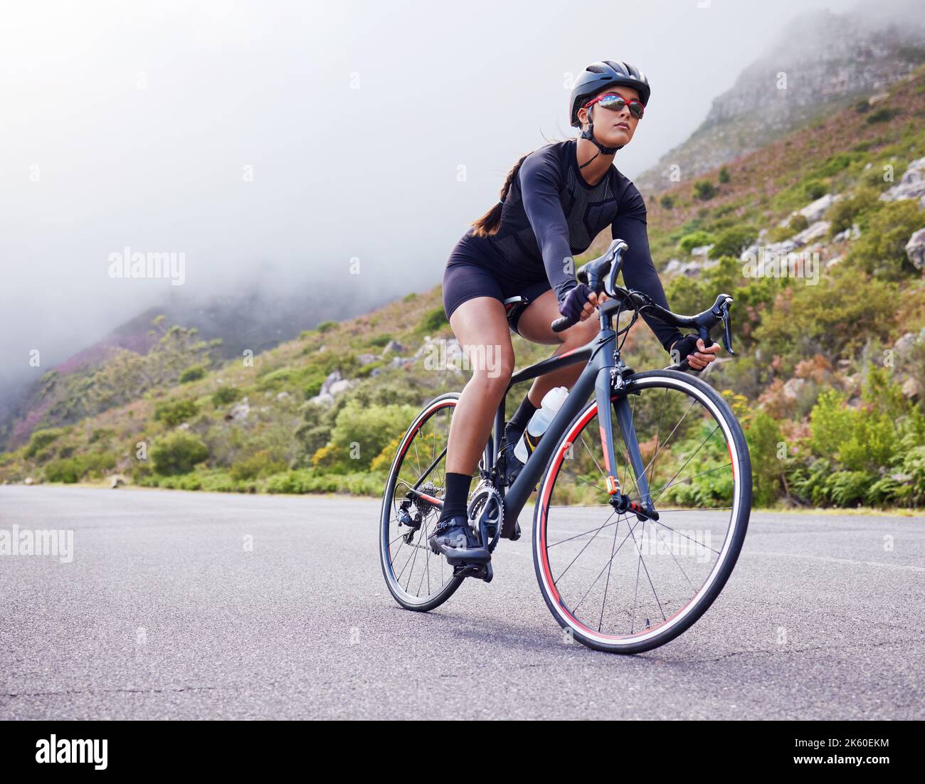 Una giovane atletica in bicicletta all'aperto. Donna sportiva indossando casco e occhiali mentre si guida una bicicletta su una strada lungo la montagna per l'esercizio Foto Stock
