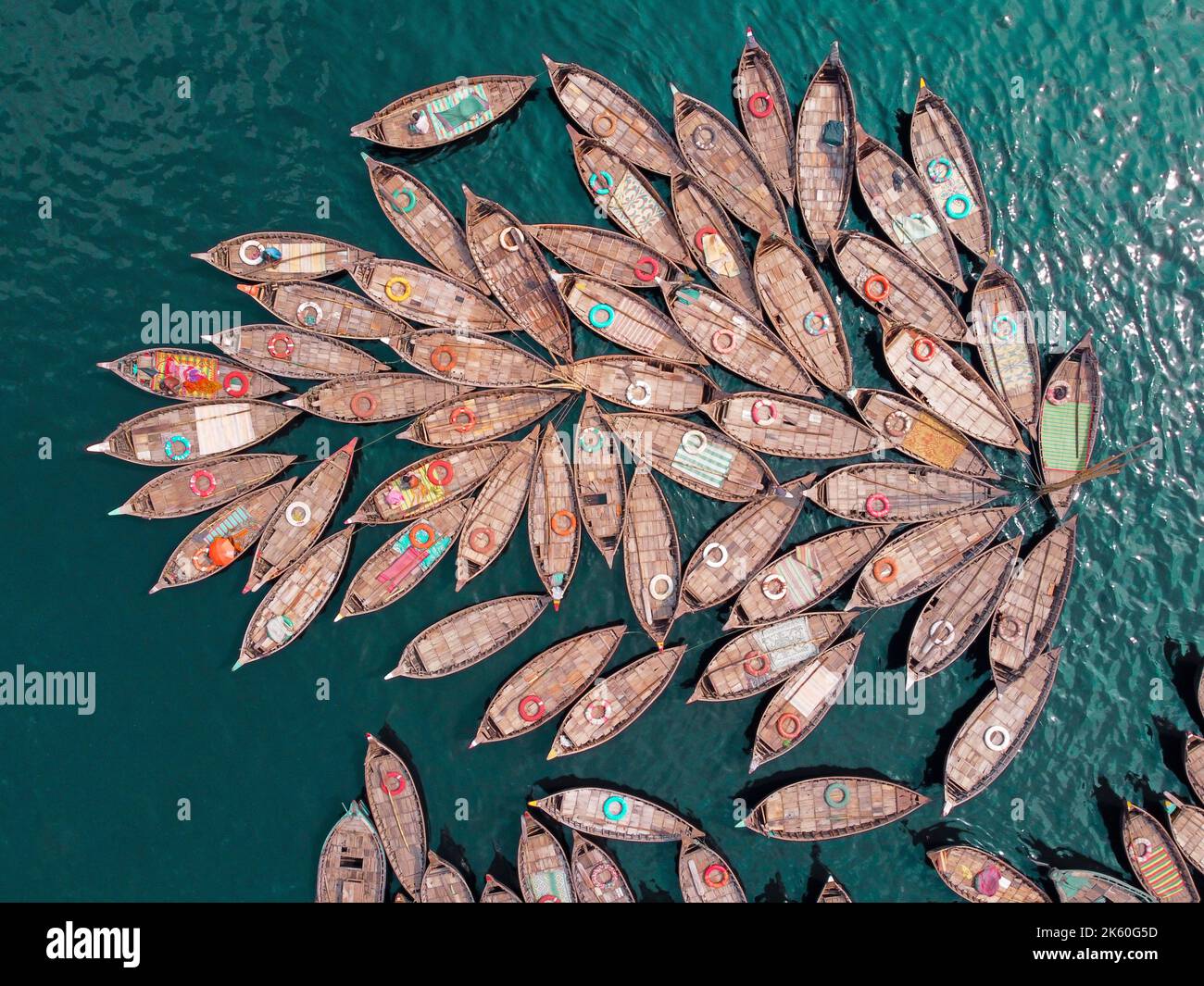 Dhaka, Dhaka, Bangladesh. 11th Ott 2022. Una flotta di barche in legno, che assomigliano ai petali di fiori, attende per i pendolari del traghetto attraverso il fiume Buriganga per lavorare in un porto fluviale importante a Dhaka, Bangladesh, mentre i barcaioli legano insieme le barche in un modello fiorito e ottenere quaranta verri davanti all'ora di punta pomeridiana. Lavorano 16 ore al giorno e ottengono meno di Â £ 5 per questo. Quindi, si riposano ogni volta che hanno la possibilità di alleviare la fatica delle lunghe ore di lavoro. Durante quel periodo, la maggior parte delle barche sono legate insieme tranne alcune e il numero di passeggeri è più basso rispetto a t Foto Stock