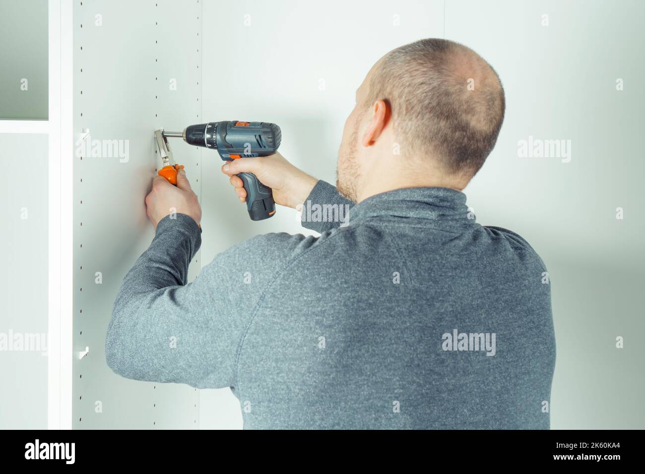 Vite maschio per inserire il supporto in plastica in una serie di fori per fissare il ripiano bianco, assemblare la credenza o l'armadio. Tiene il cacciavite con le pinze Foto Stock