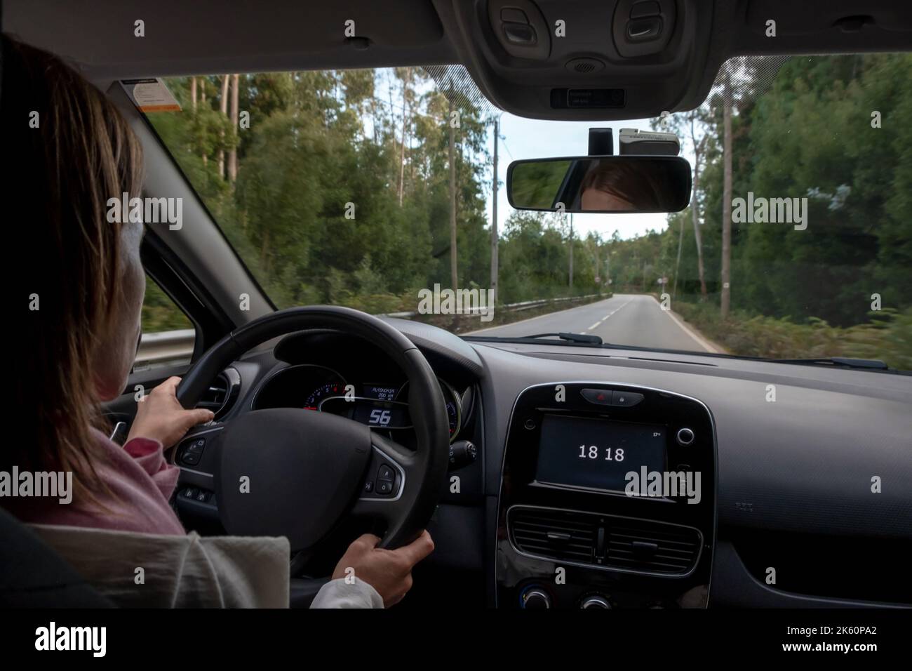 Donna che guida, vista dal sedile posteriore ad angolo basso rispetto al cruscotto principale dell'auto. Dalla POV del sedile posteriore lato passeggero. Foto Stock