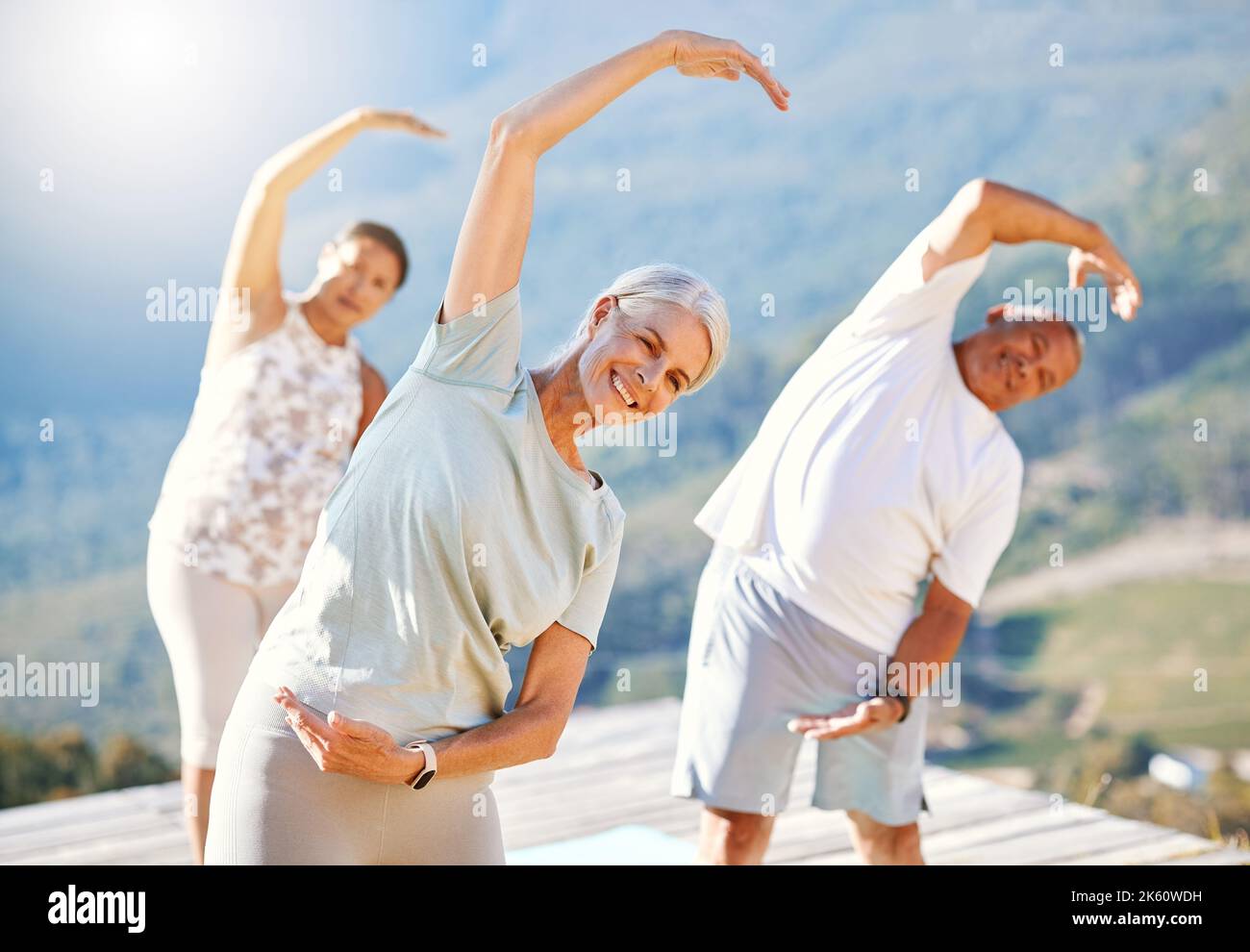 Gruppo di persone anziane che si allungano con le mani sopra la testa all'aperto. La gente matura felice che fa l'esercitazione di yoga nella natura in una giornata di sole. Lezione di yoga Foto Stock