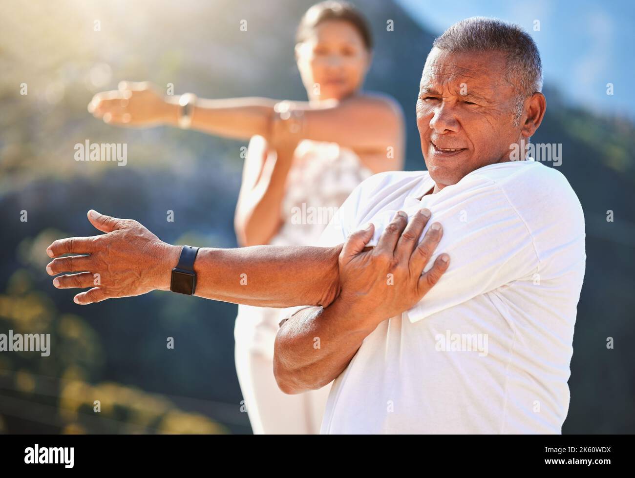 Uomo anziano che allunga le braccia mentre si esercita all'aperto in una giornata di sole. Persone mature che praticano lo yoga insieme in natura rimanendo sane e attive Foto Stock