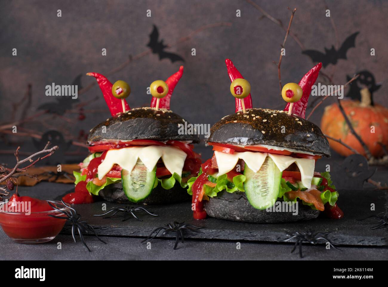 Due divertenti hamburger neri di mostro con pesce, pane tostato, cetriolo, pomodoro, ketchup, olive occhi e corna peperoncino. Cucina creativa di Halloween Foto Stock