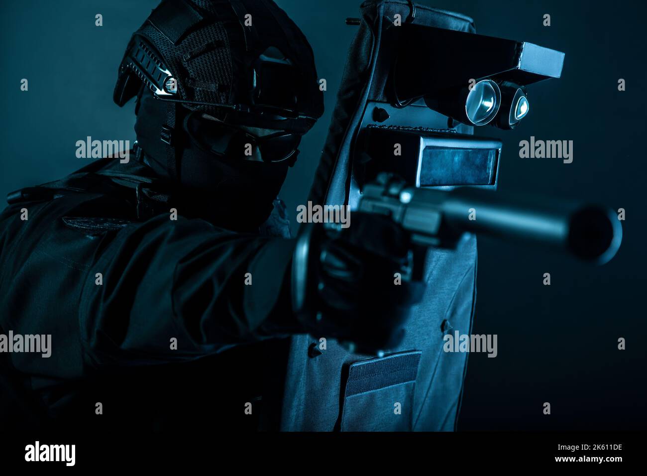 Combattente delle forze speciali della polizia, membro della squadra d'assalto, ufficiale del gruppo tattico in uniformi nere, puntando con la pistola silenziata mentre si nasconde dietro, coprendosi con lo scudo balistico, colorato Foto Stock