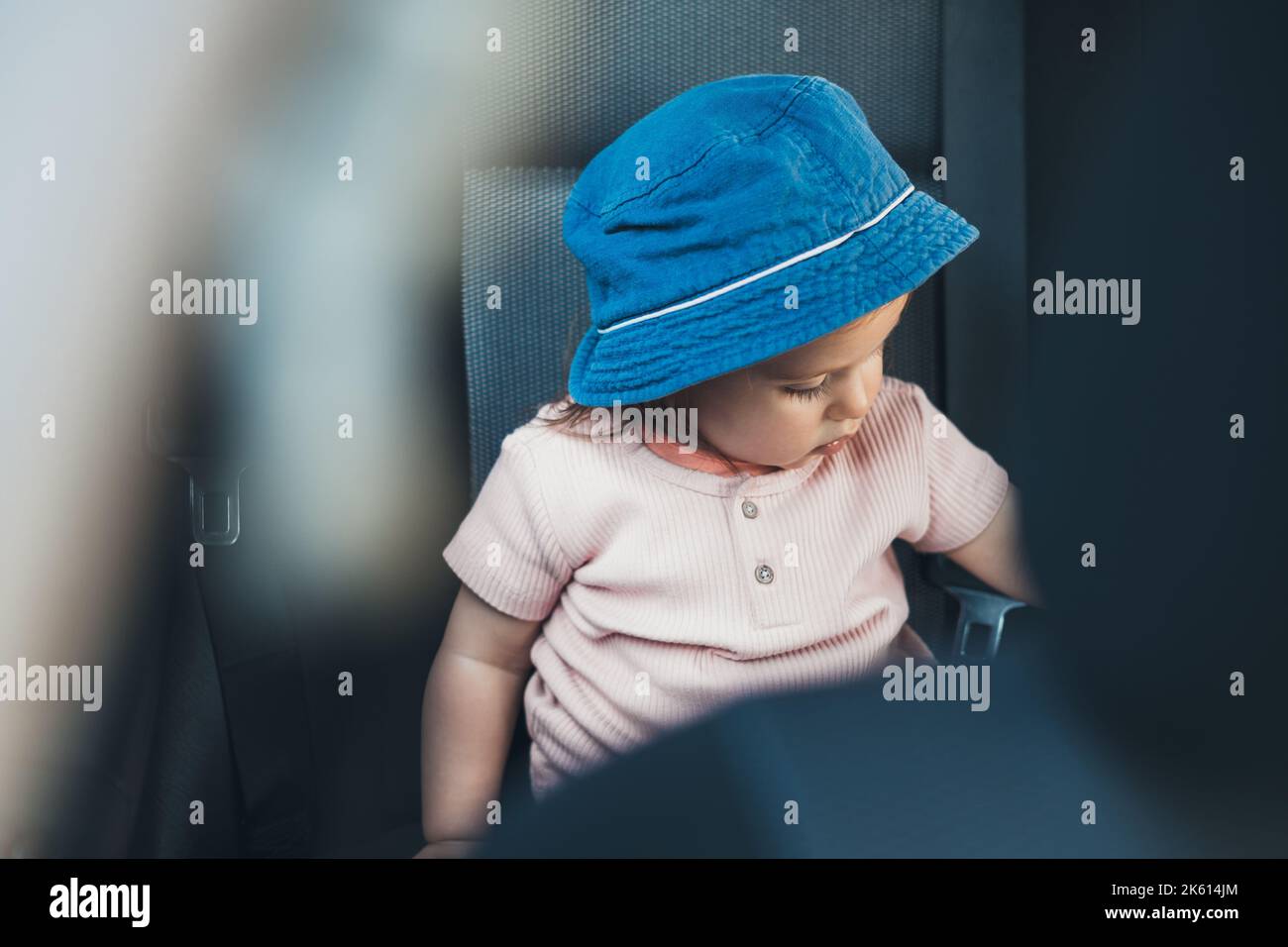 Ragazza piccola felice in seggiolino auto per bambini, con cappello blu. Famiglia, trasporto, viaggio su strada e concetto di persone - ragazza felice in sicurezza di guida sedile Foto Stock